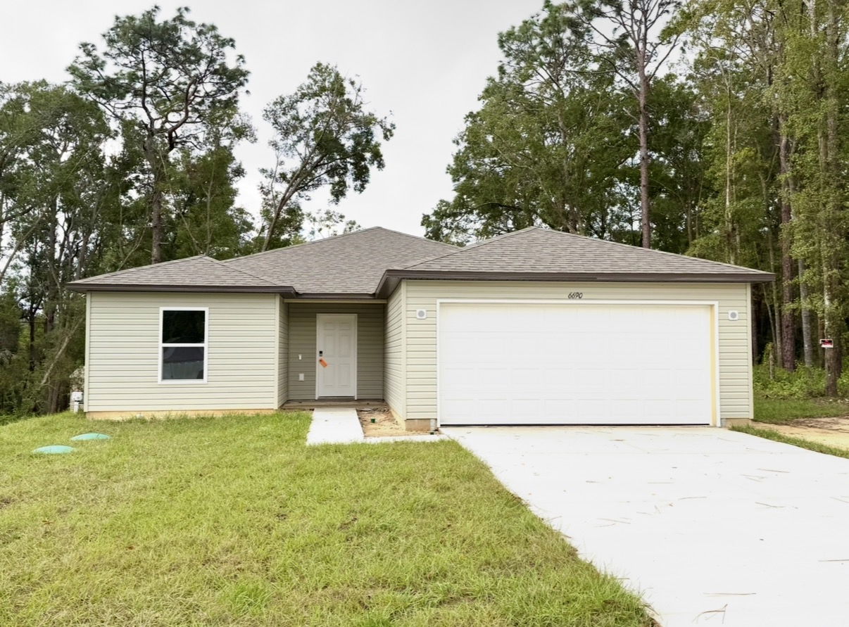 Newly constructed single-story house with a two-car garage, light siding, and surrounded by trees.