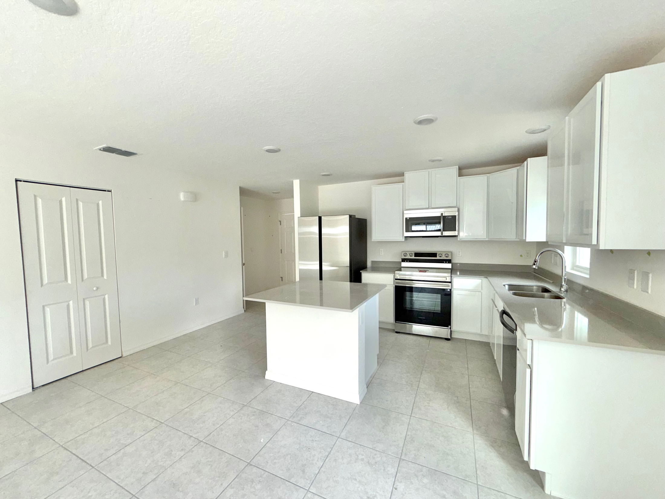 Modern kitchen with white cabinets, stainless steel appliances, and a central island, featuring tile flooring and recessed lighting.