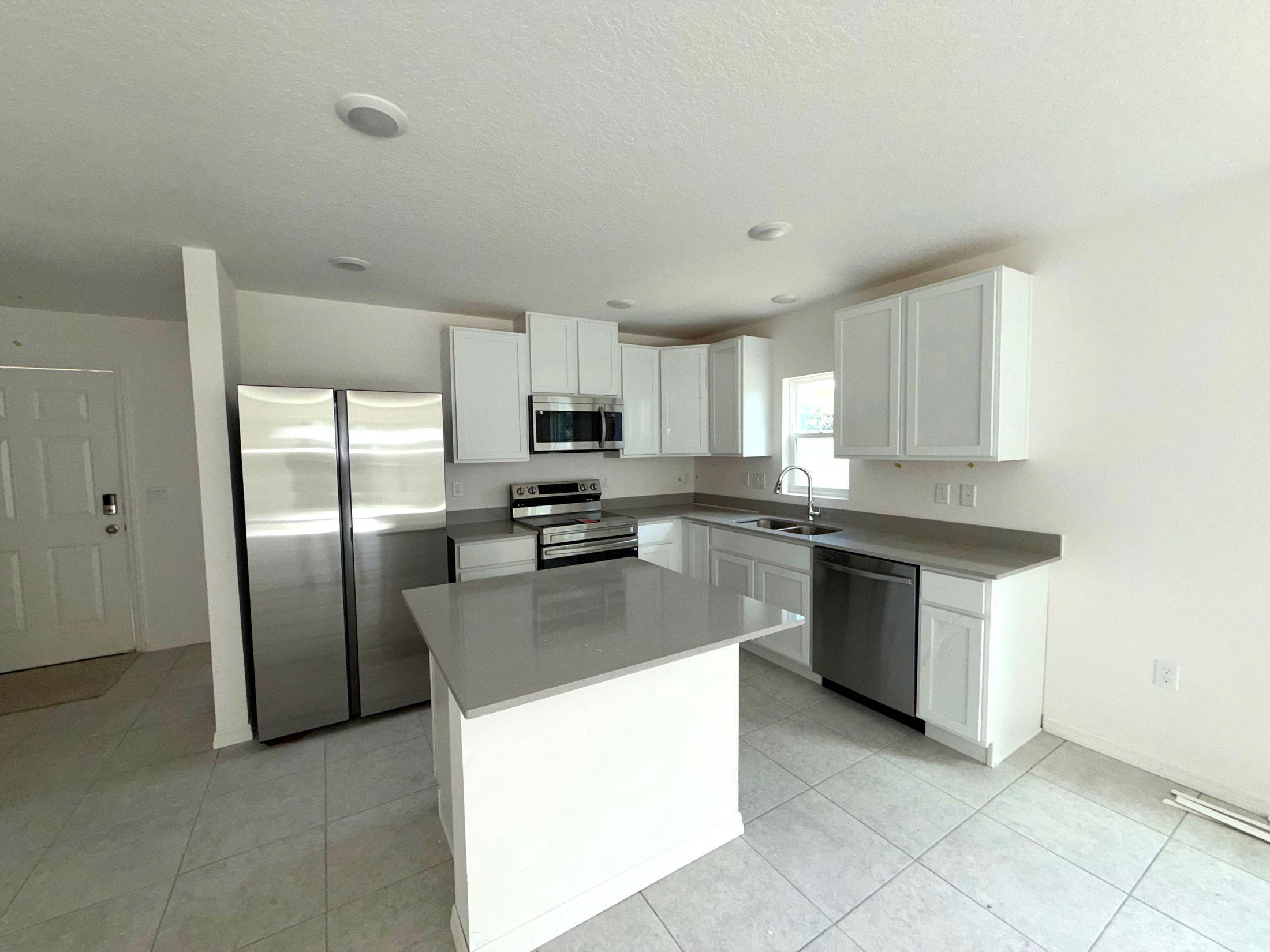 Modern kitchen with white cabinets, stainless steel appliances, and a sleek grey countertop and island.