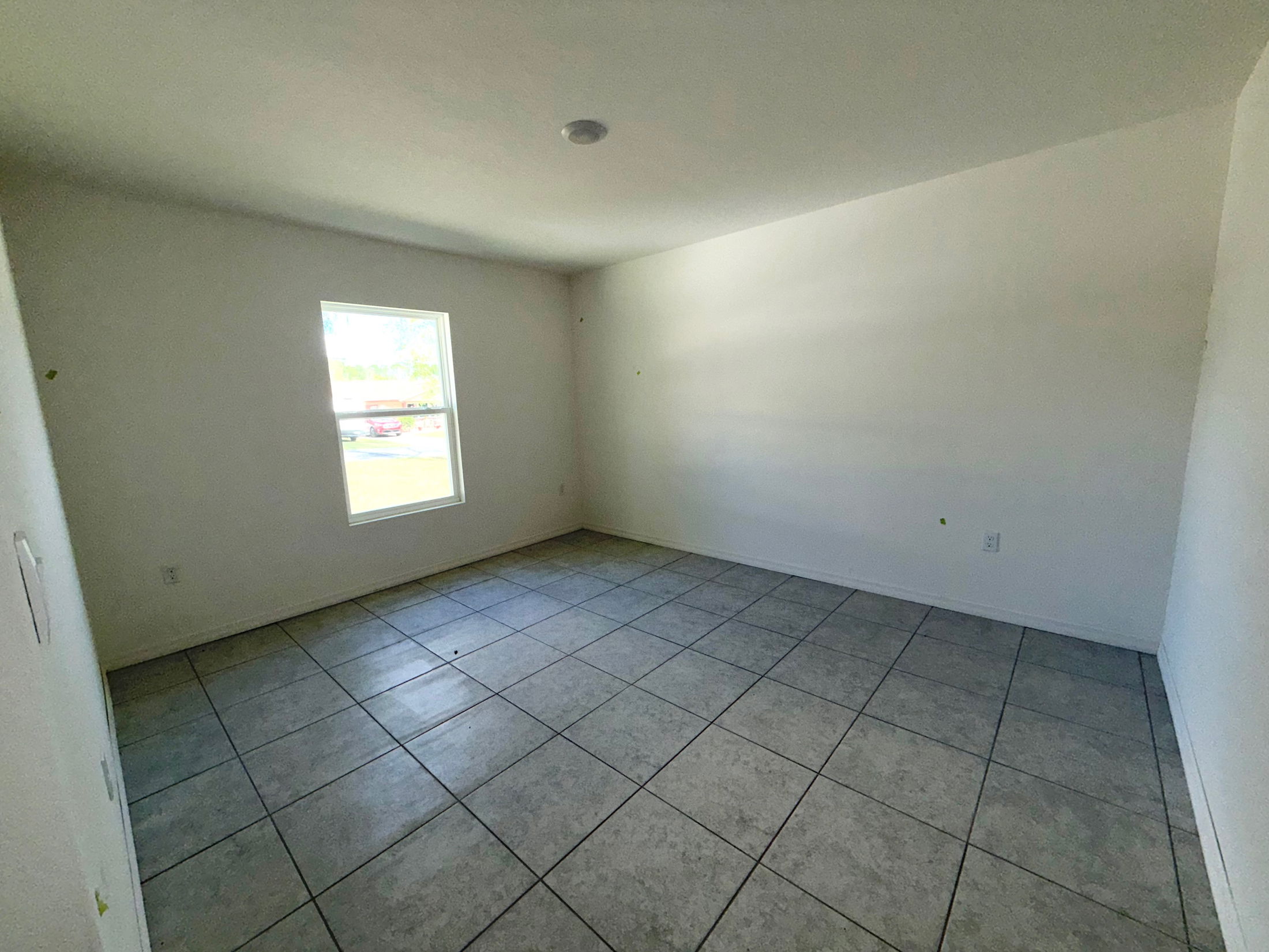 Empty room with white walls, a window, and tiled flooring, ideal for home decoration or remodeling projects.