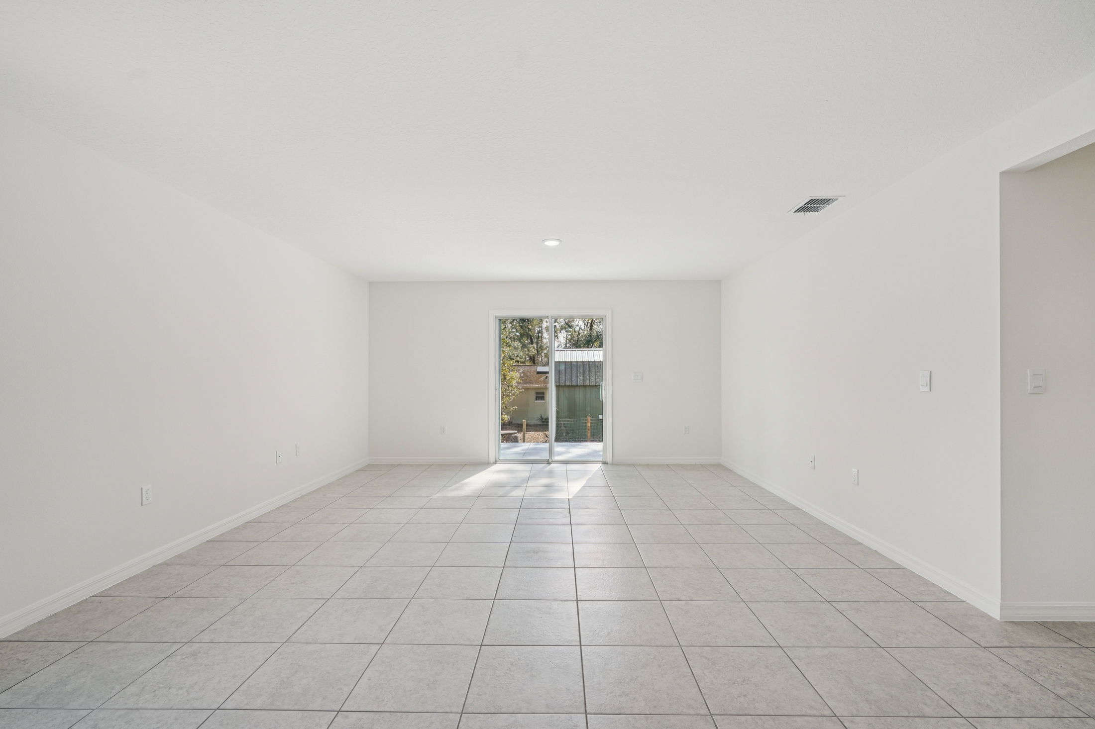 Bright and airy living room with tile flooring and sliding glass doors leading to an outdoor space.