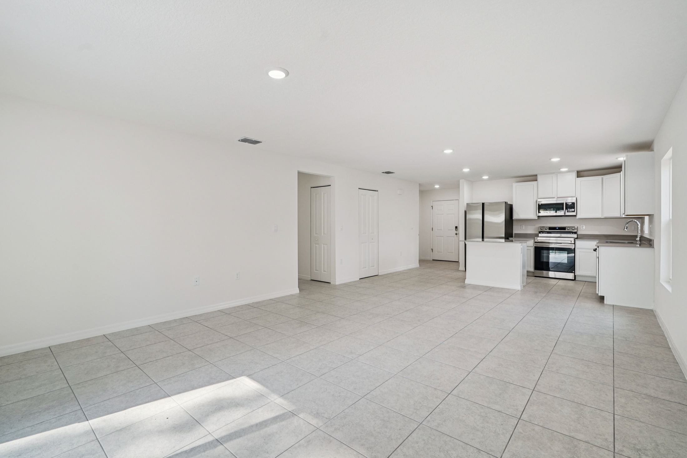 Modern open-concept kitchen and living area with tile flooring and stainless steel appliances in a bright, airy space.