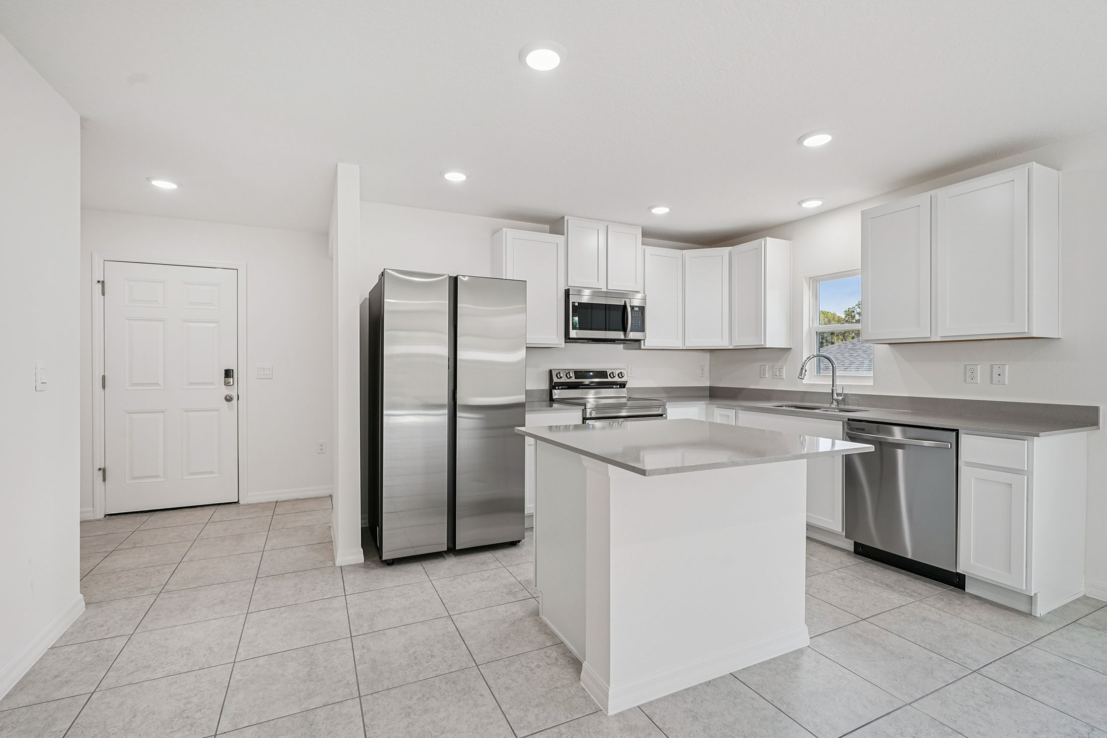 Modern kitchen design featuring stainless steel appliances, white cabinetry, and an open floor plan with tile flooring.