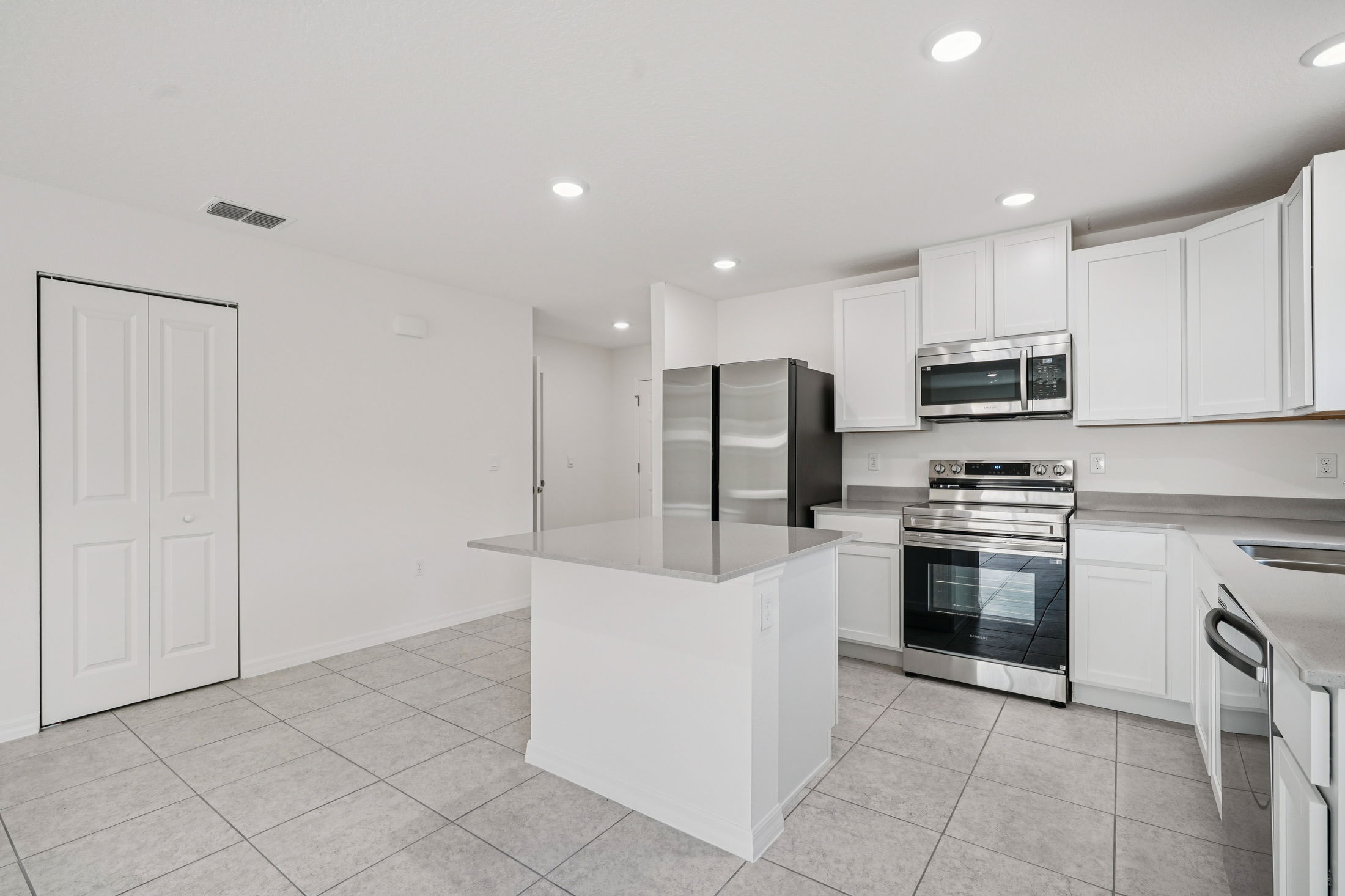 Modern white kitchen with stainless steel appliances, gray countertops, and tiled flooring in a spacious layout.