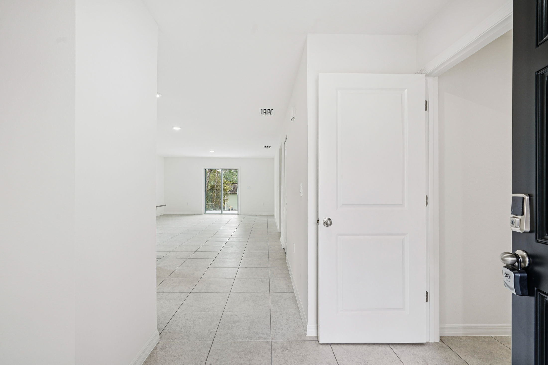Spacious and bright hallway leading to an open living area with tile flooring and large sliding glass doors.