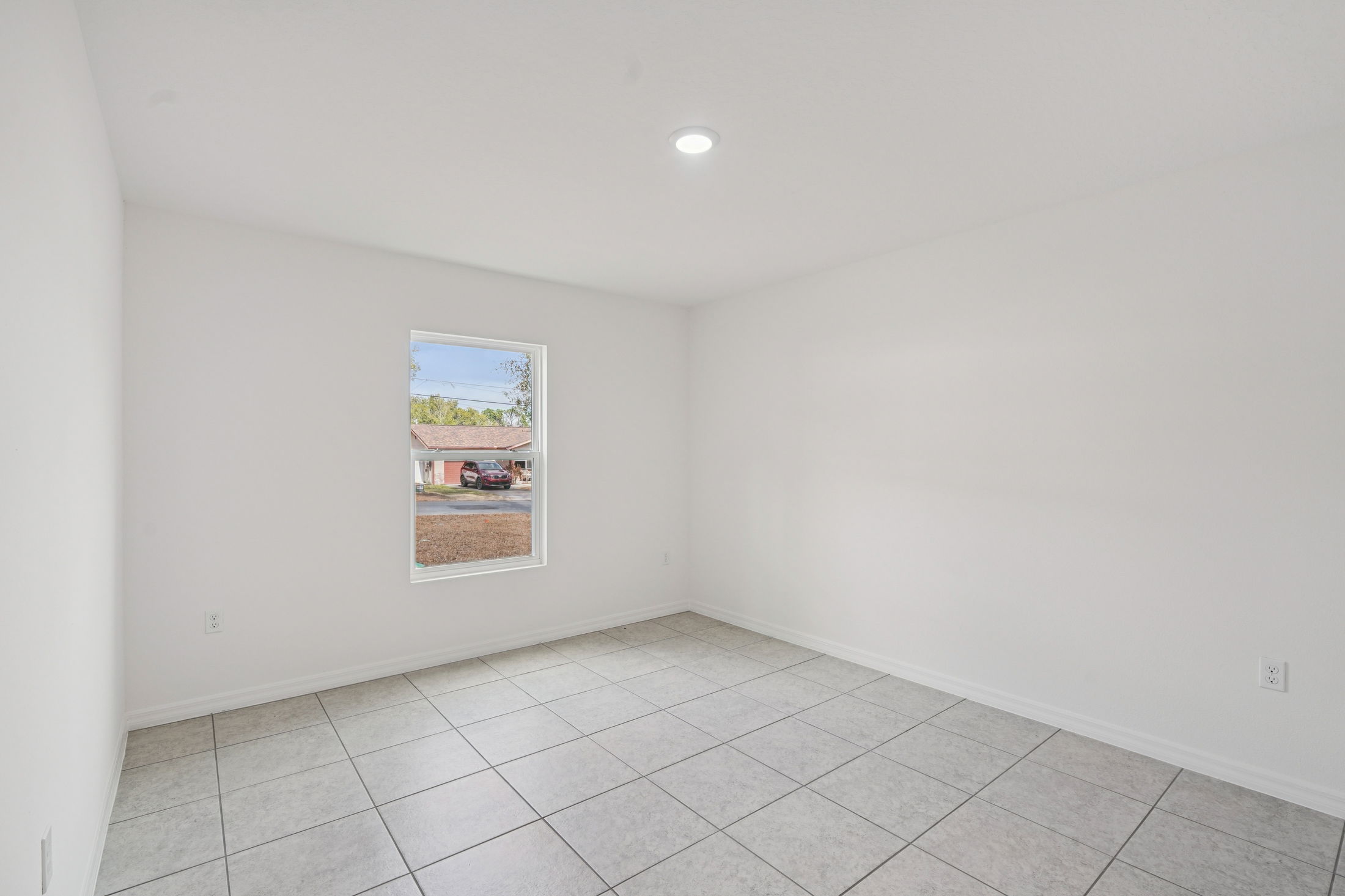 Spacious empty room with white walls and tiled flooring, featuring a window that allows natural light to enter.