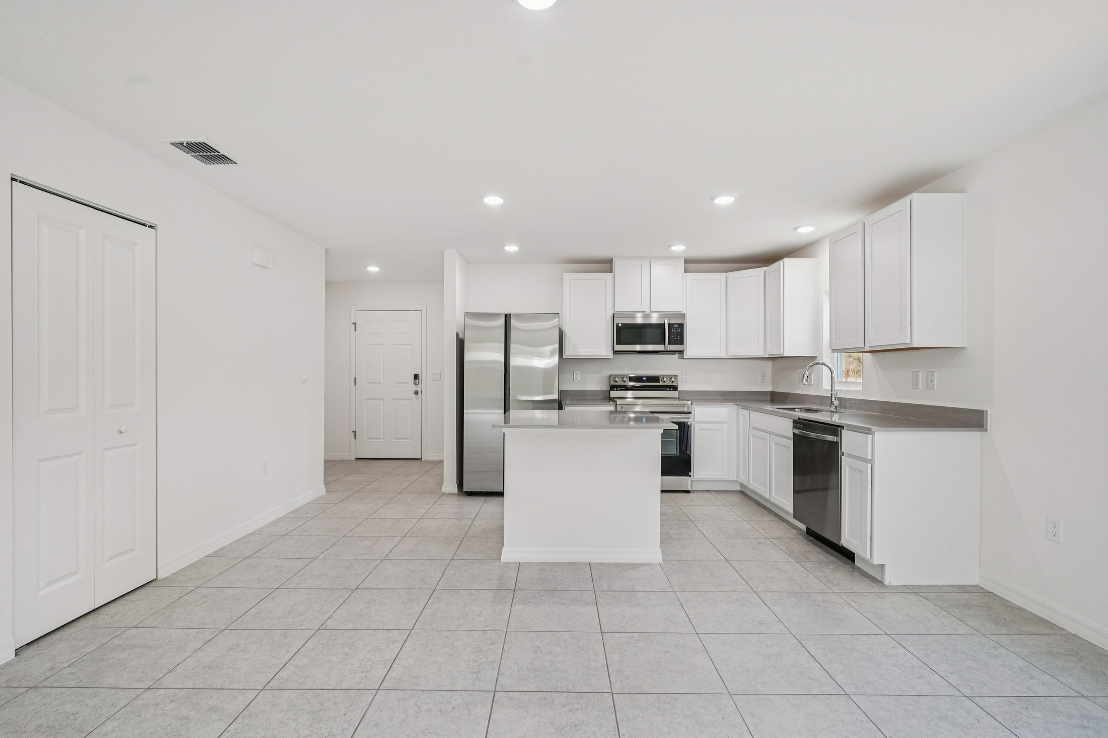Modern kitchen with stainless steel appliances, white cabinets, and tile flooring in an open-concept layout.
