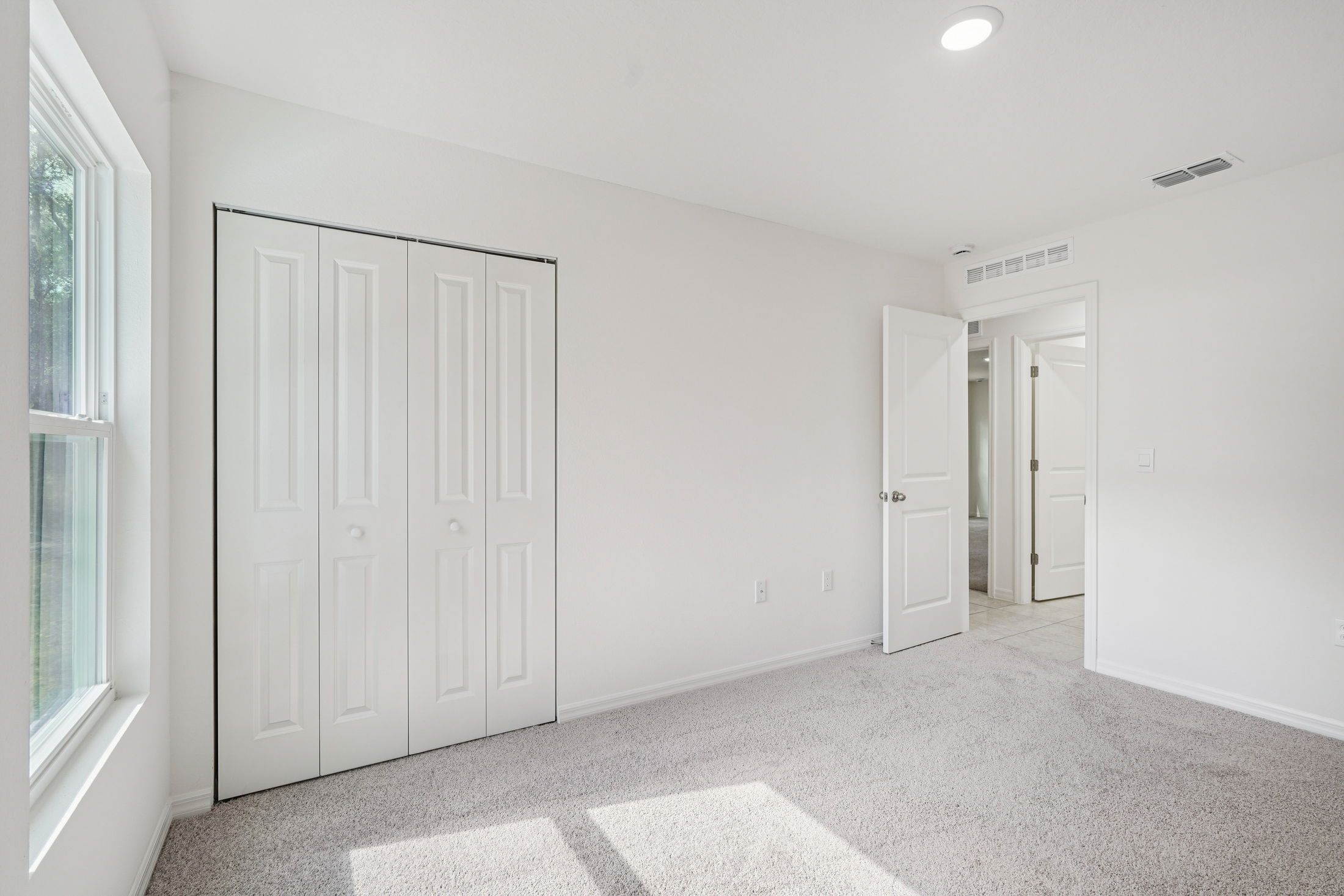 Bright and airy bedroom featuring white walls, carpeted flooring, and a double closet with sliding doors.