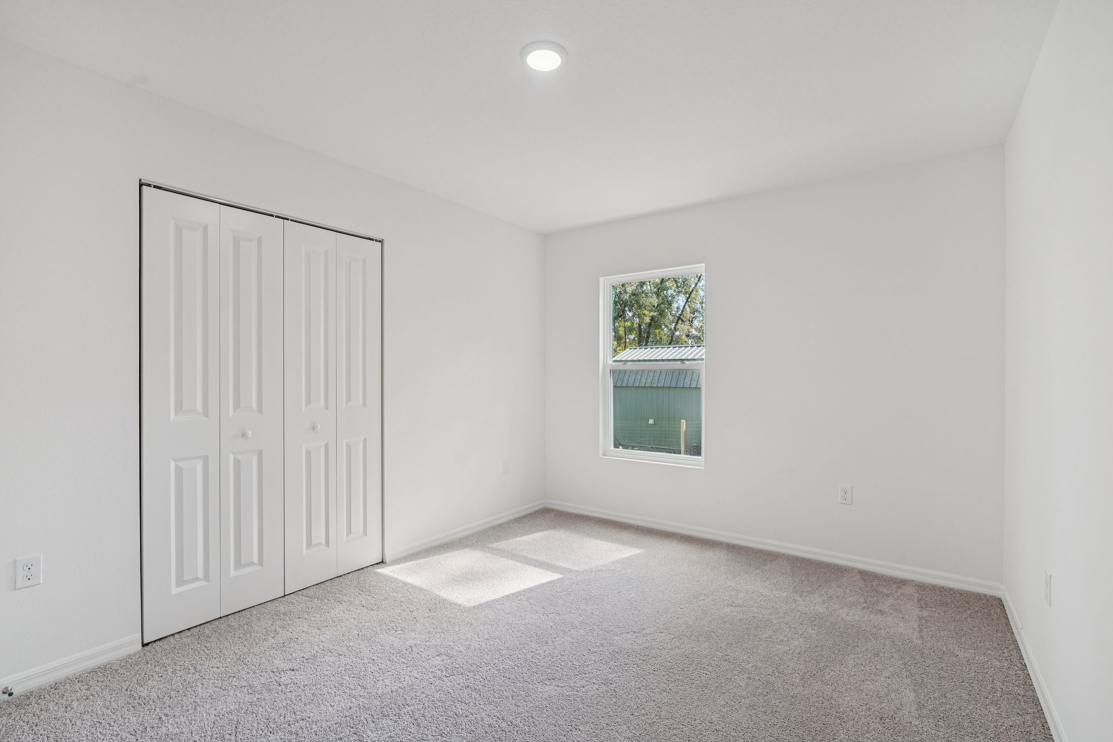 Bright, empty bedroom featuring light gray carpet, white walls, and a closet with sliding doors.