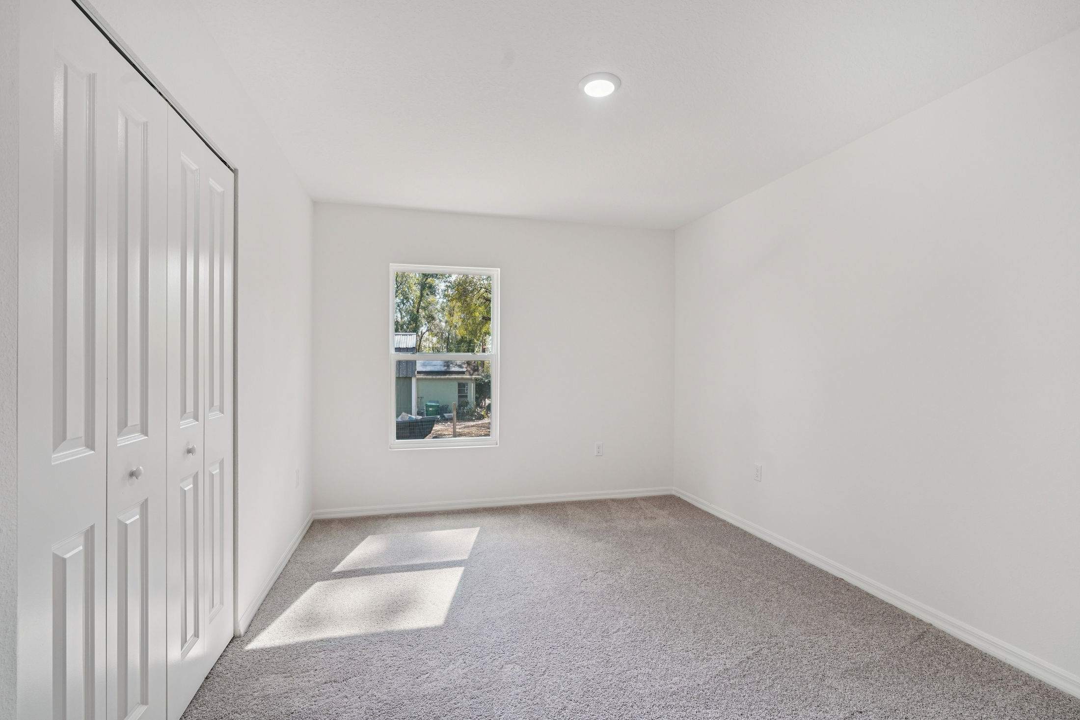 Bright and spacious bedroom featuring beige carpeting, white walls, and a large window overlooking a serene outdoor view.