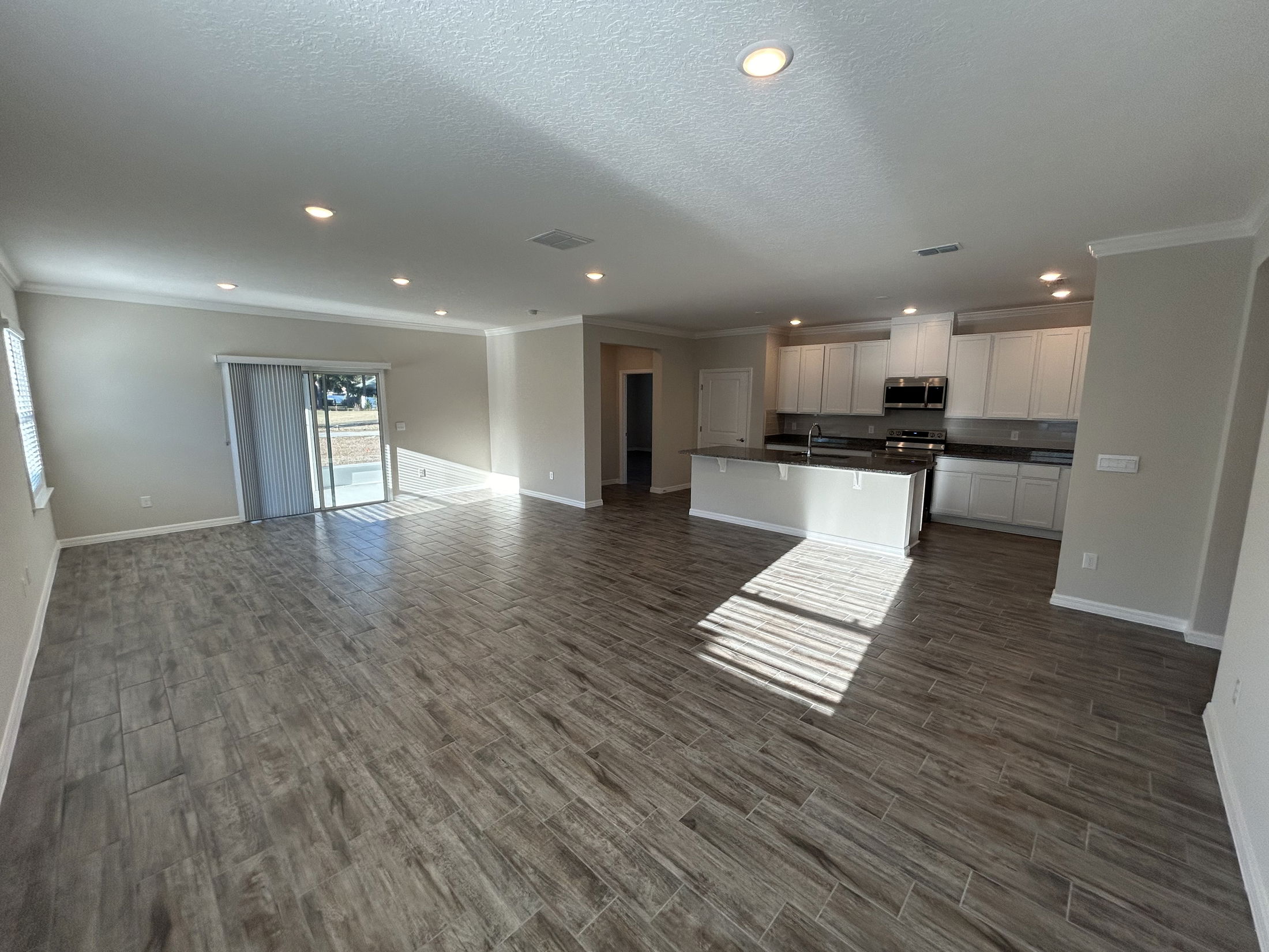 Spacious modern living room with hardwood flooring and an open kitchen layout featuring stainless steel appliances.