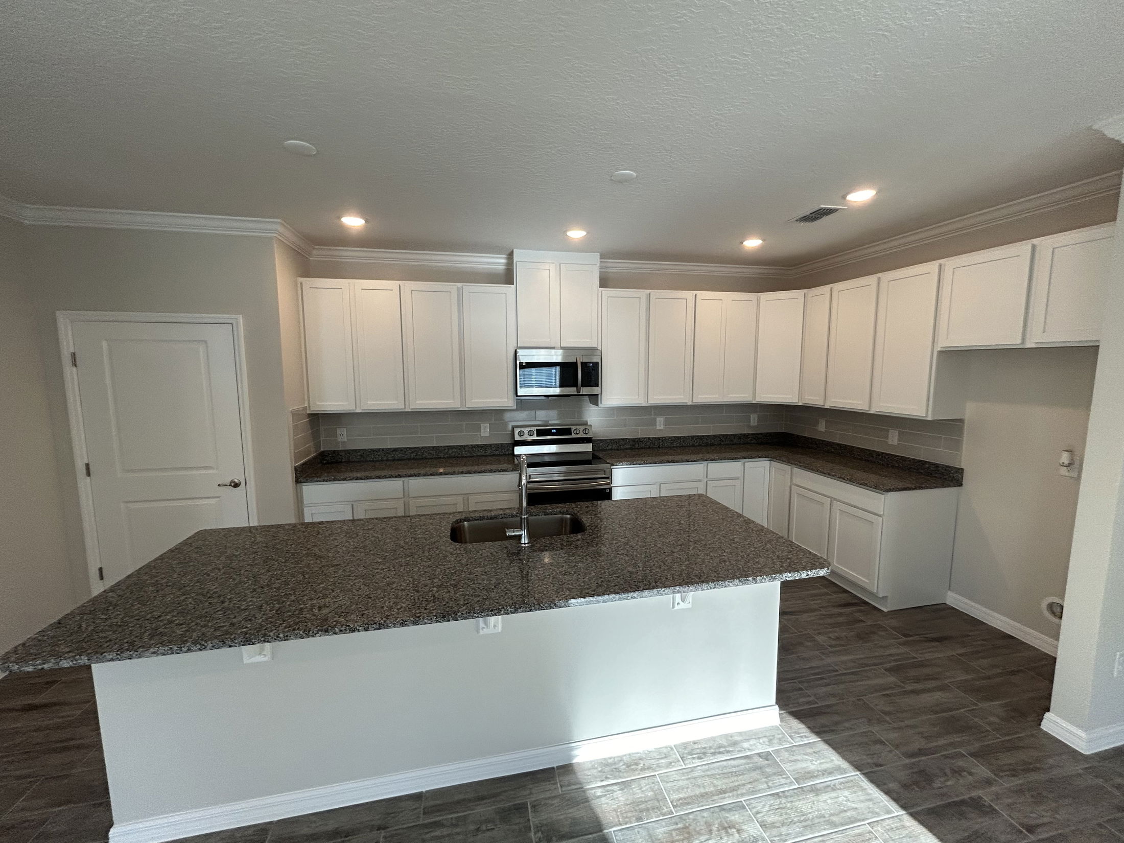 Modern kitchen featuring white cabinets, granite countertops, stainless steel appliances, and an open floor plan.