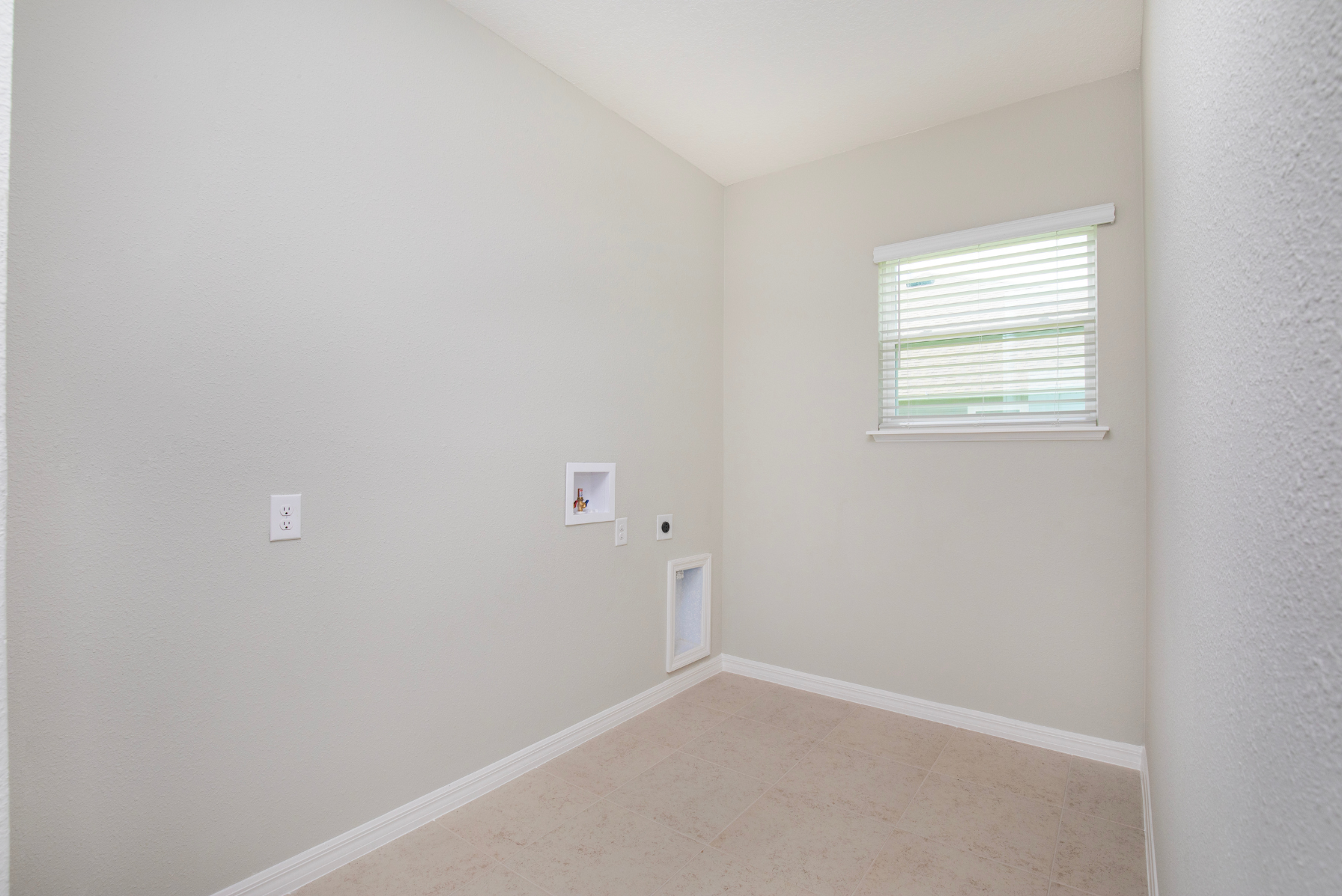 Empty laundry room with beige walls, tiled floor, and a window with blinds.