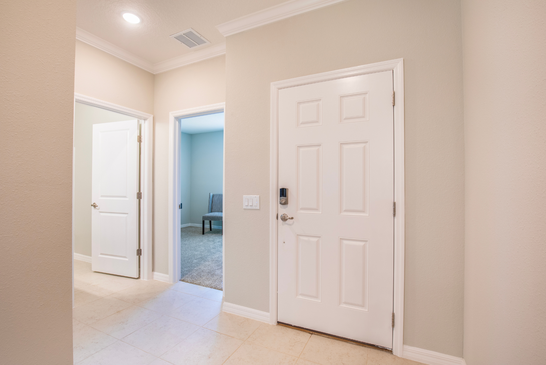 Bright, modern hallway with tiled floor featuring open doors leading to carpeted rooms and a closed white front door.