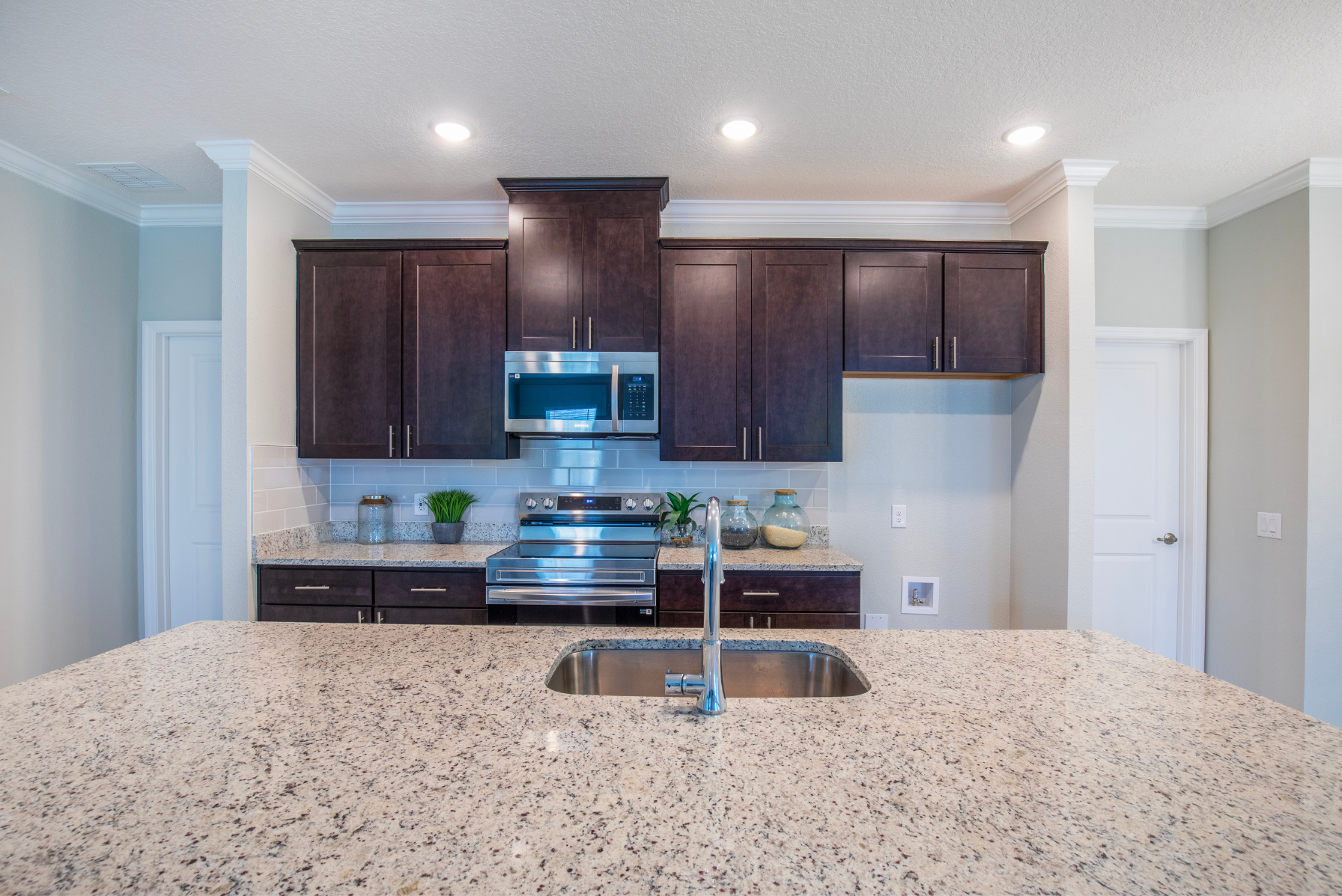 Modern kitchen with dark wood cabinets, stainless steel appliances, and a granite island with a built-in sink.