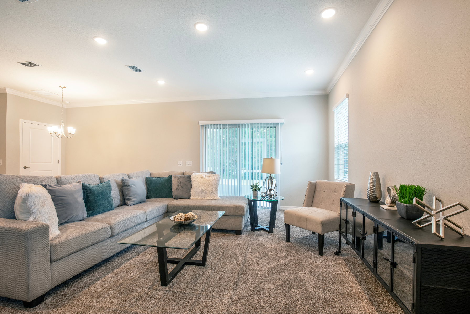 Modern living room with a spacious gray sectional couch, glass coffee table, and elegant lighting, creating a cozy and inviting atmosphere.