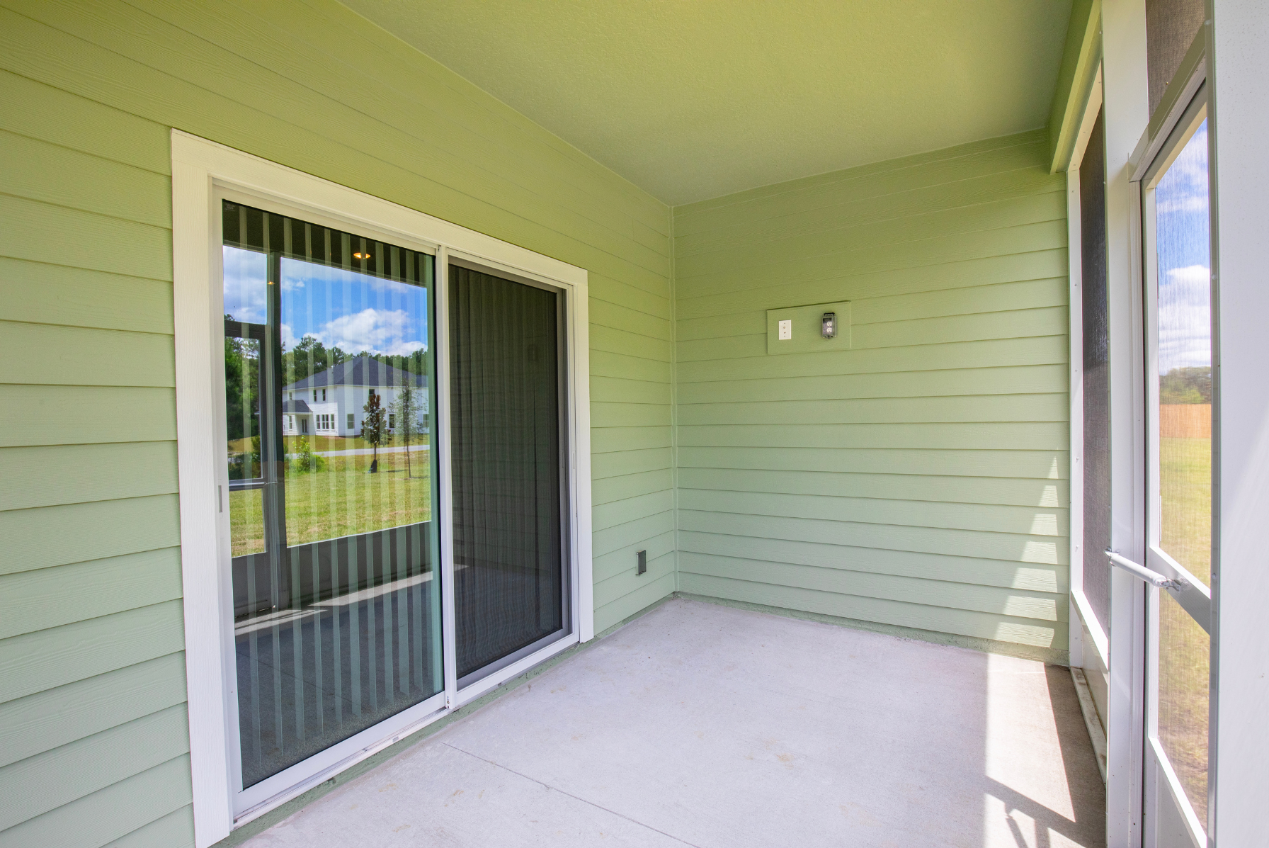 Covered patio with green siding and sliding glass doors overlooking a grassy backyard.