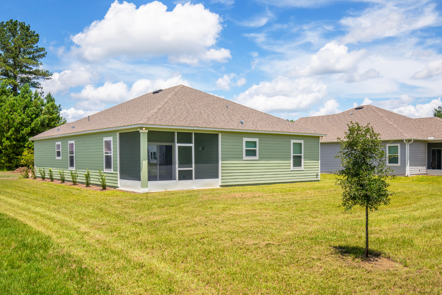 Single-story green house with a screened porch and landscaped yard under a blue sky.