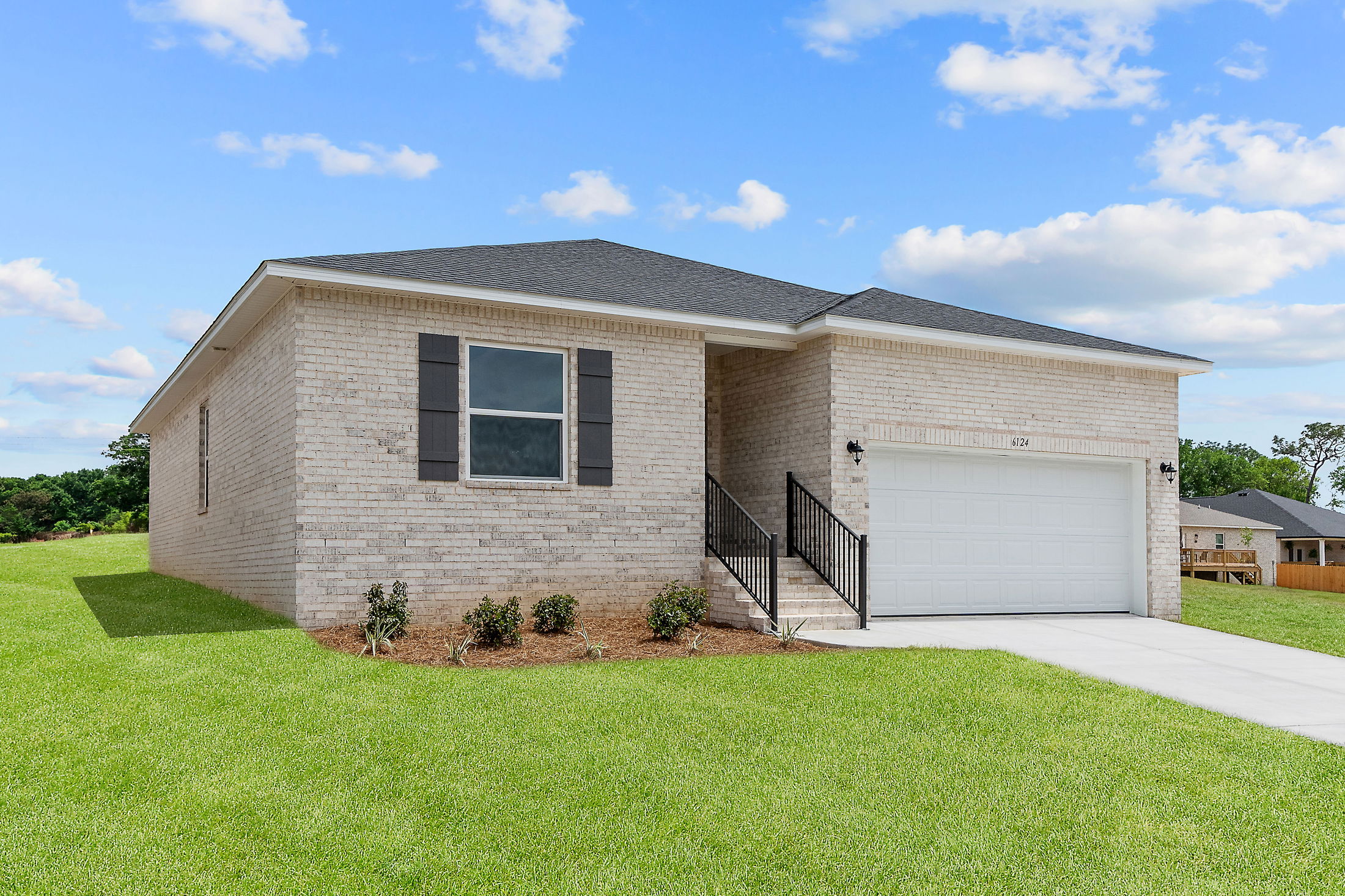 Modern one-story brick house with a garage and manicured lawn under a blue sky.