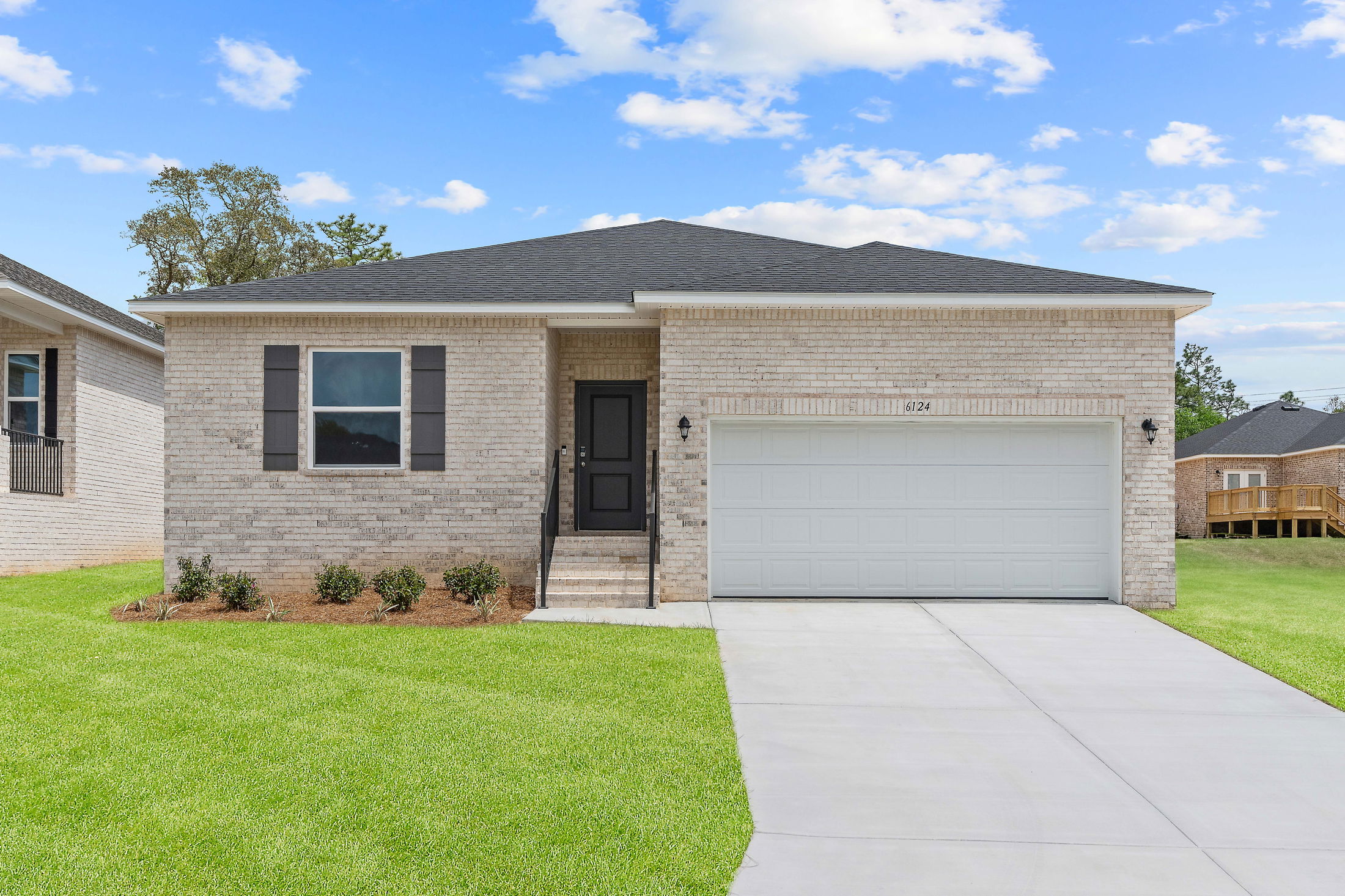 Single-story brick house with a spacious front lawn and attached garage under a clear blue sky.