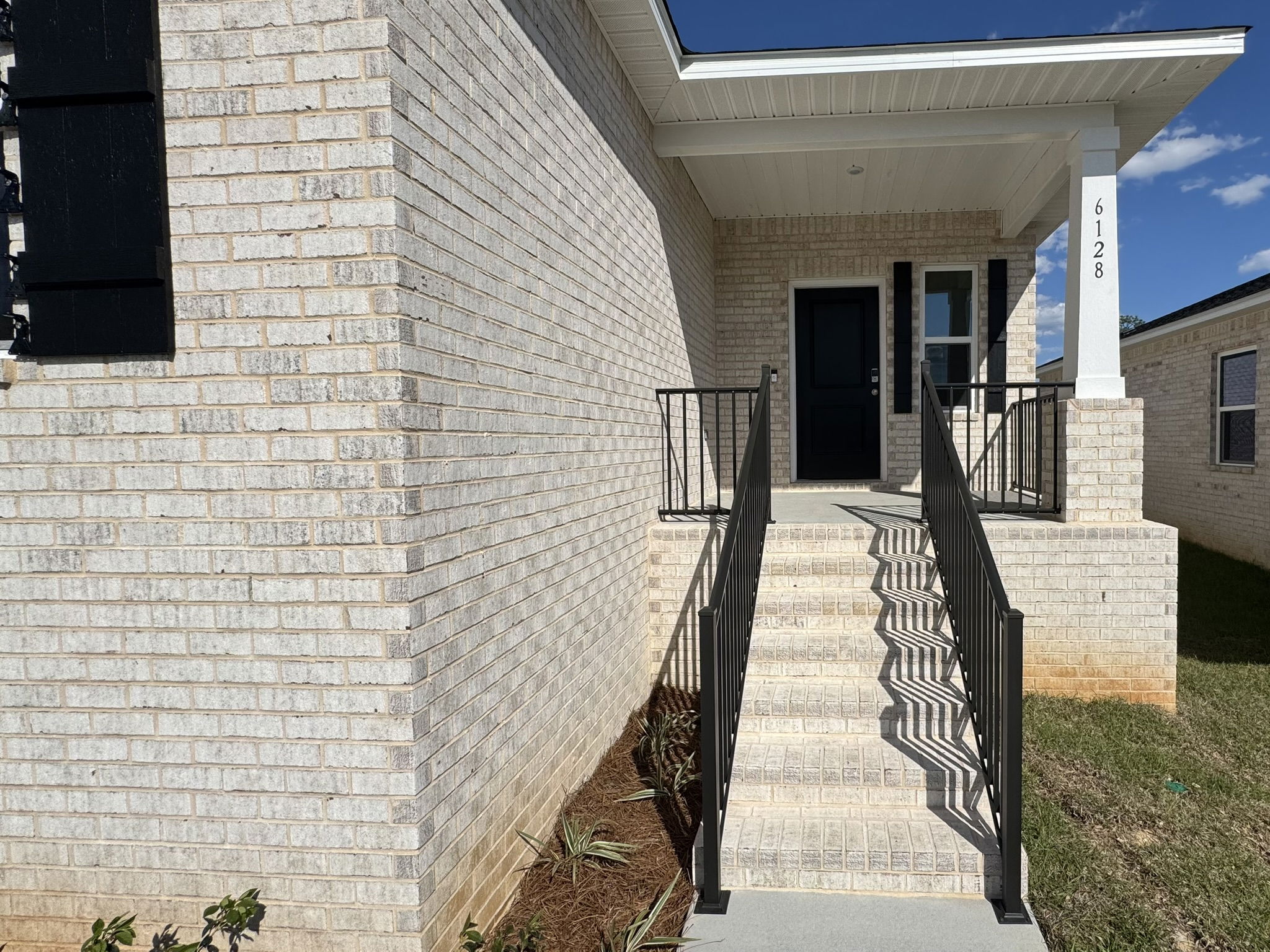 Front porch of a modern white brick house with black metal railings and a dark door.