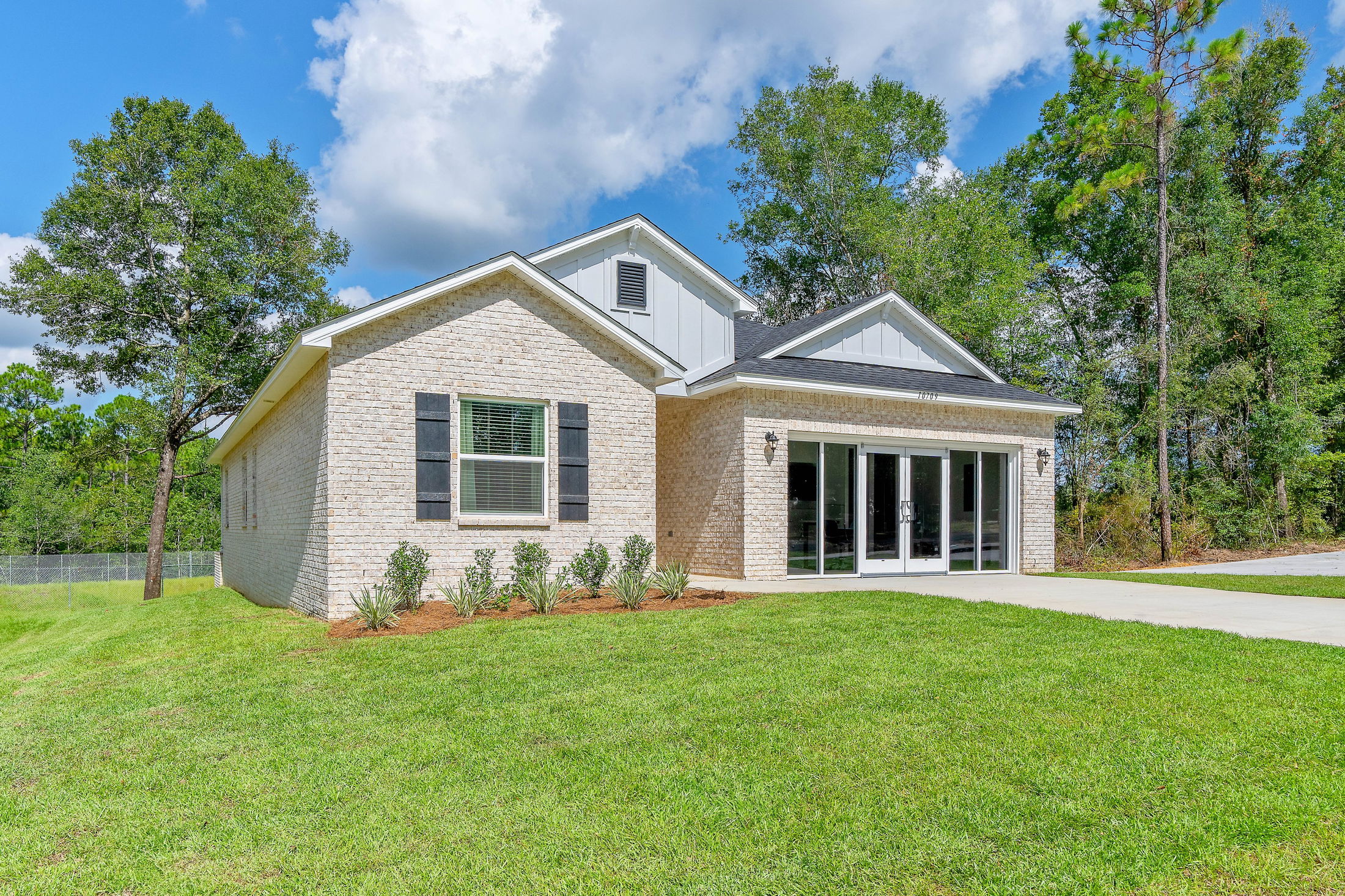 Modern single-story white brick house with lush green lawn and large trees under a clear blue sky.