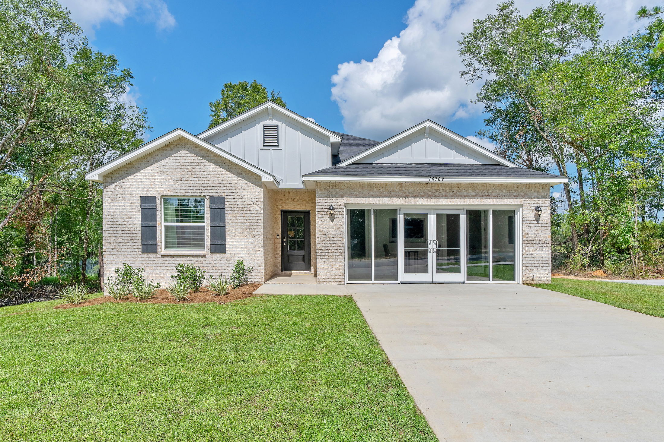 A modern, single-story white brick house with a neatly manicured lawn and a spacious driveway under a clear blue sky.