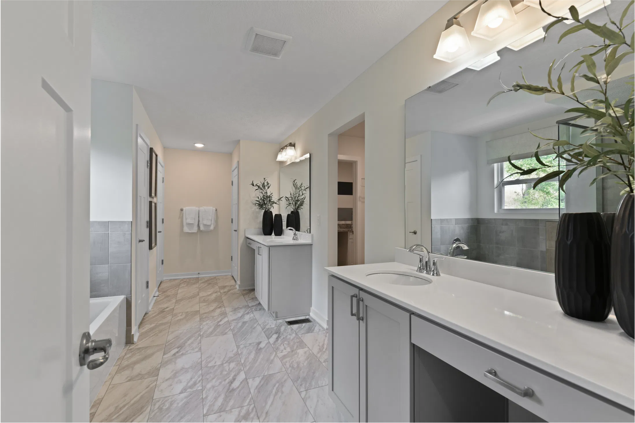 Modern bathroom with dual sinks, sleek gray cabinetry, large mirrors, and a marble-tiled floor.