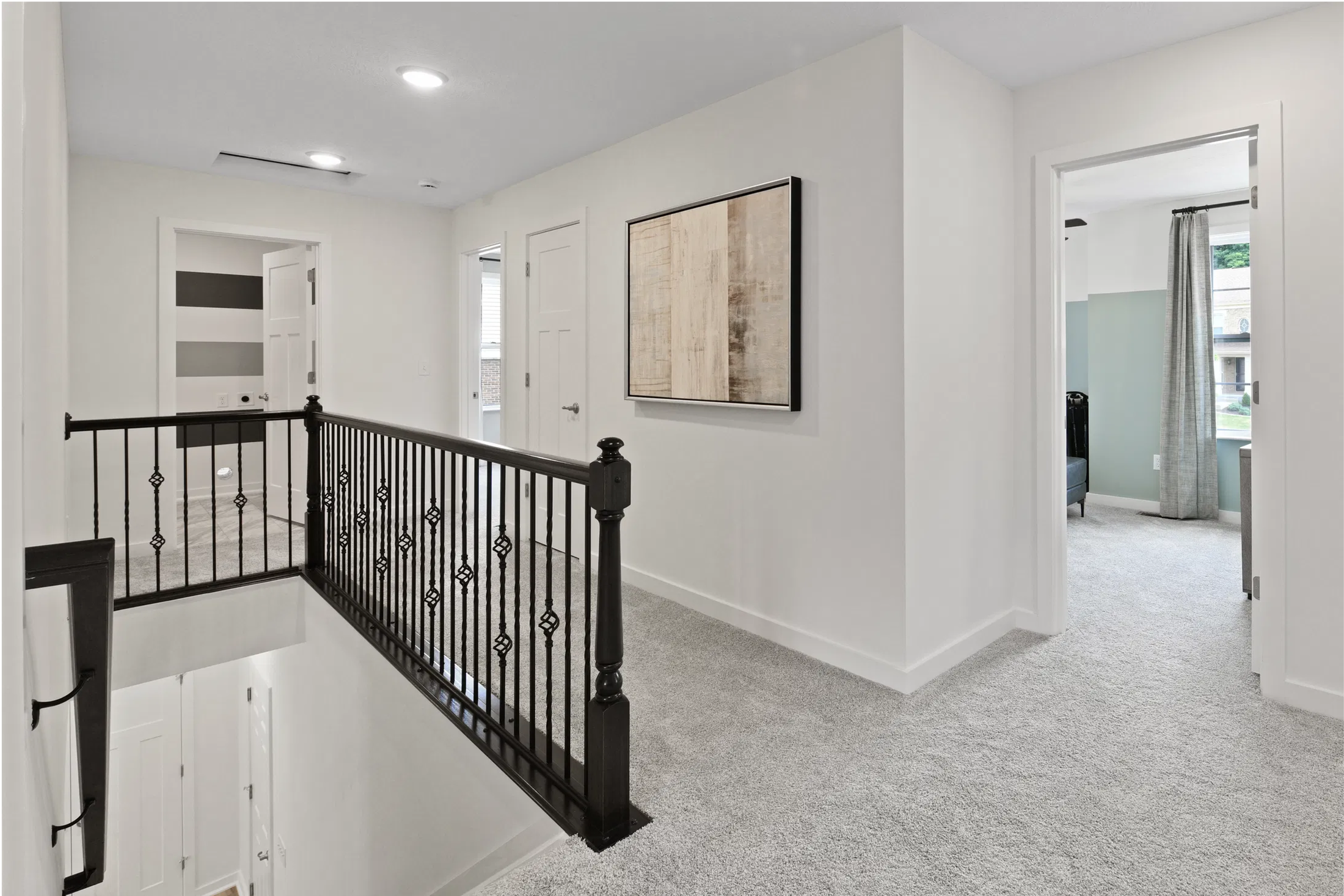 Upstairs hallway with modern black railing, carpet flooring, and abstract artwork on the wall.