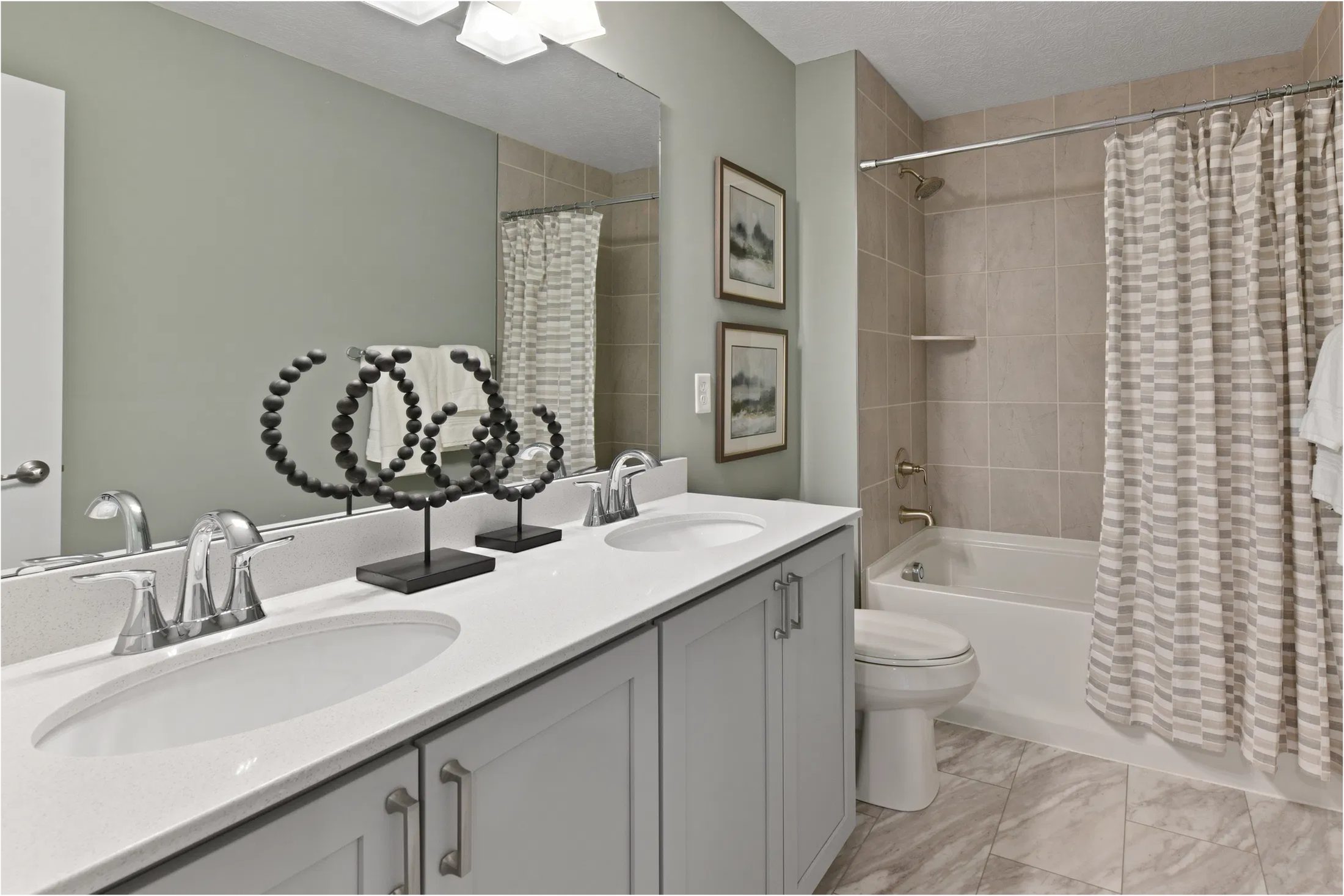 Modern bathroom with dual sinks, elegant fixtures, and a tiled bathtub with a striped shower curtain.