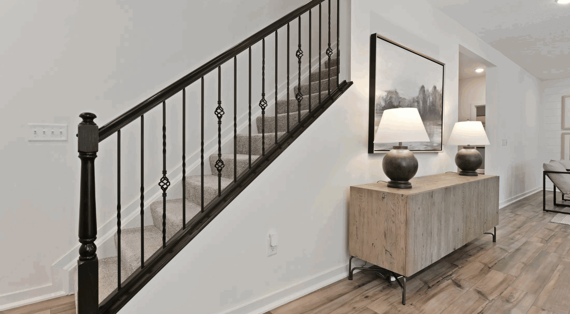 Stylish modern staircase with dark iron railing and a wooden console table with lamps in a bright interior.