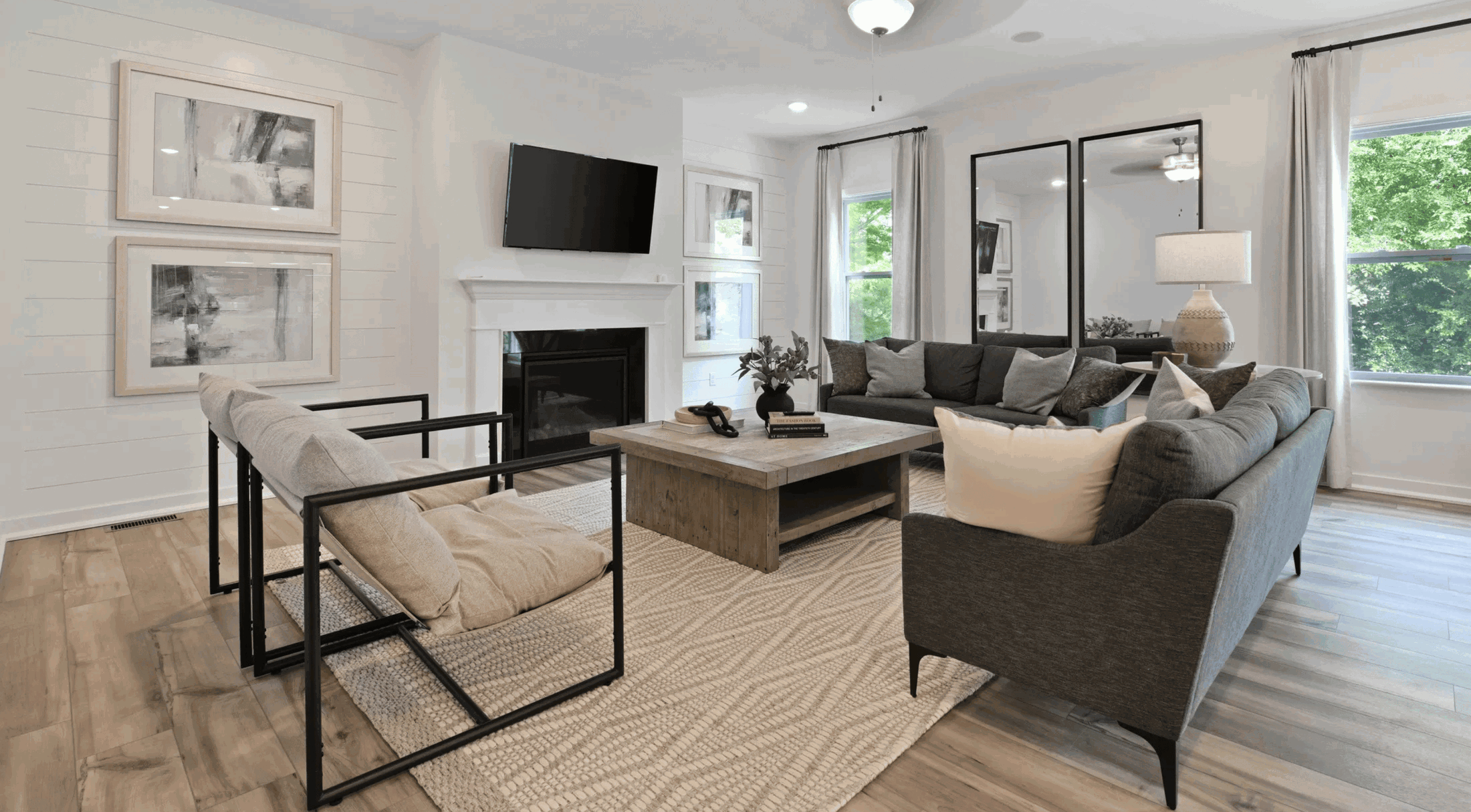 Modern living room with a gray sectional sofa, wooden coffee table, wall-mounted TV, abstract artwork, and cozy decor.
