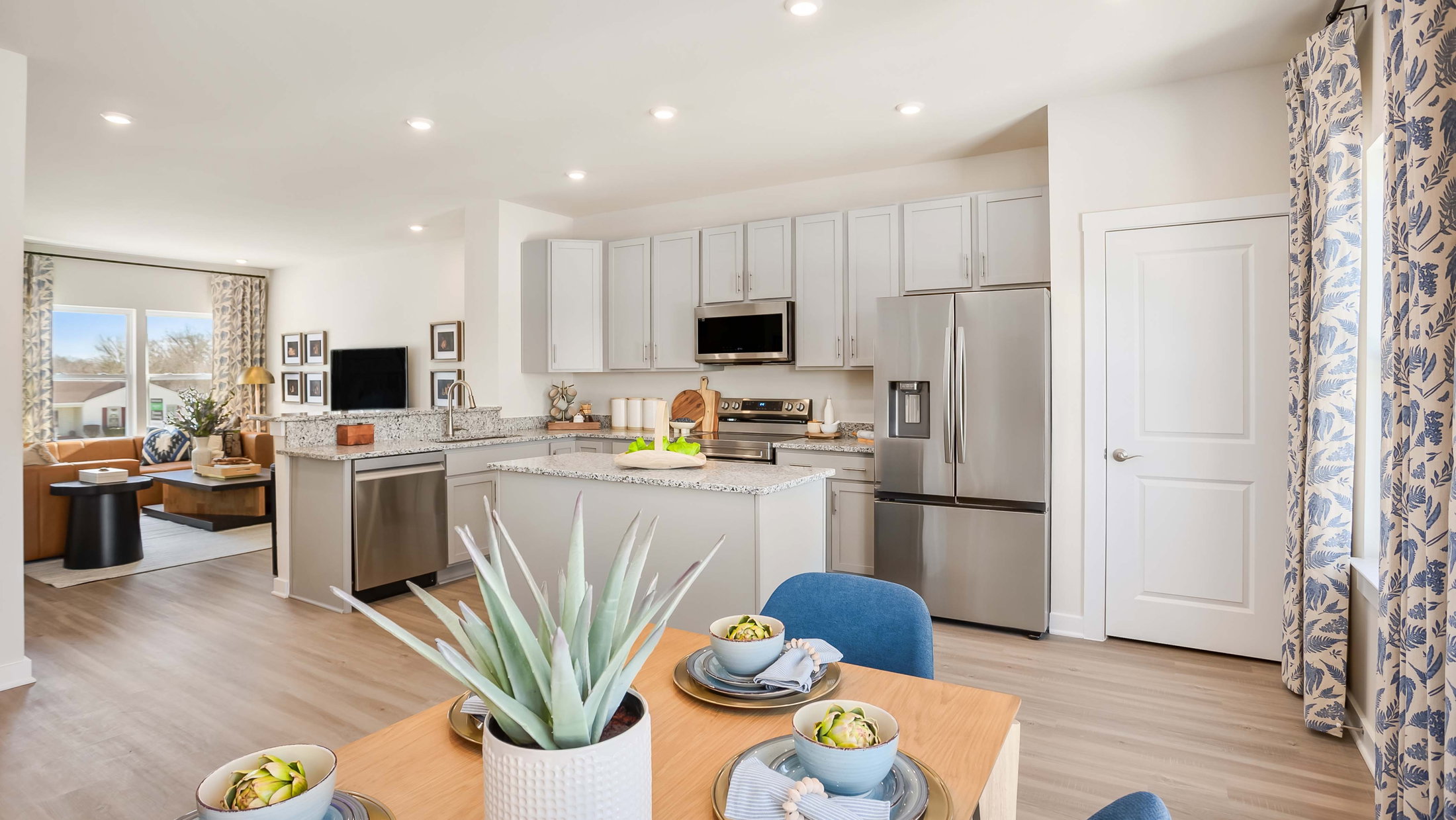 Bright, modern kitchen featuring granite countertops, stainless steel appliances, and a dining area set with bowls of fruit.