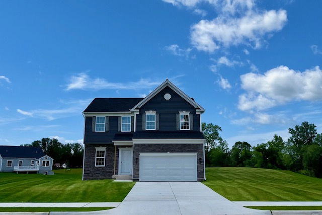 Two-story suburban house with a dark facade and white garage, set against a clear blue sky and a neatly manicured lawn.