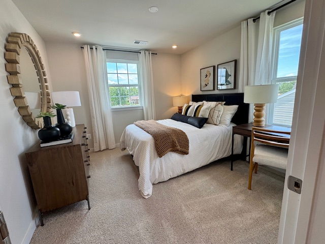 Cozy and modern bedroom featuring a neatly made bed, decorative pillows, a round wall mirror, and natural light from two windows with curtains.