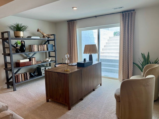 Modern home office with a wooden desk, stylish bookcase, beige chairs, and natural light from a large sliding glass door.