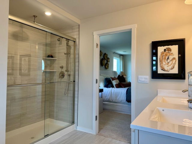 Modern bathroom with a glass shower and dual sinks leading into a cozy bedroom.