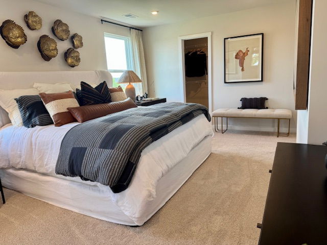Modern bedroom with a cozy upholstered bed, decorative pillows, wall art, and a bench, featuring neutral tones and natural light.