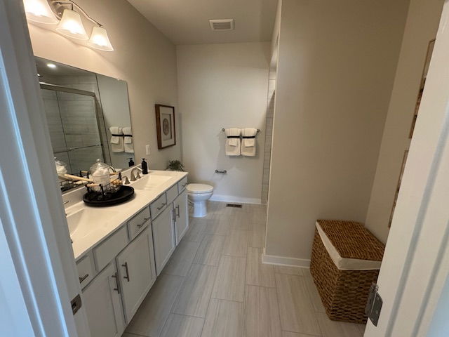 Modern bathroom with white cabinets, large mirror, tile flooring, and a wicker laundry basket.
