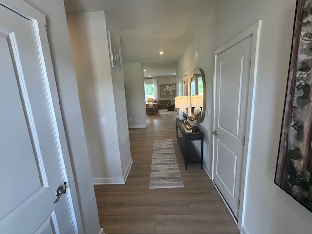 Modern hallway with wooden floors, a wall mirror, and a console table with lamps leading to a bright living room.