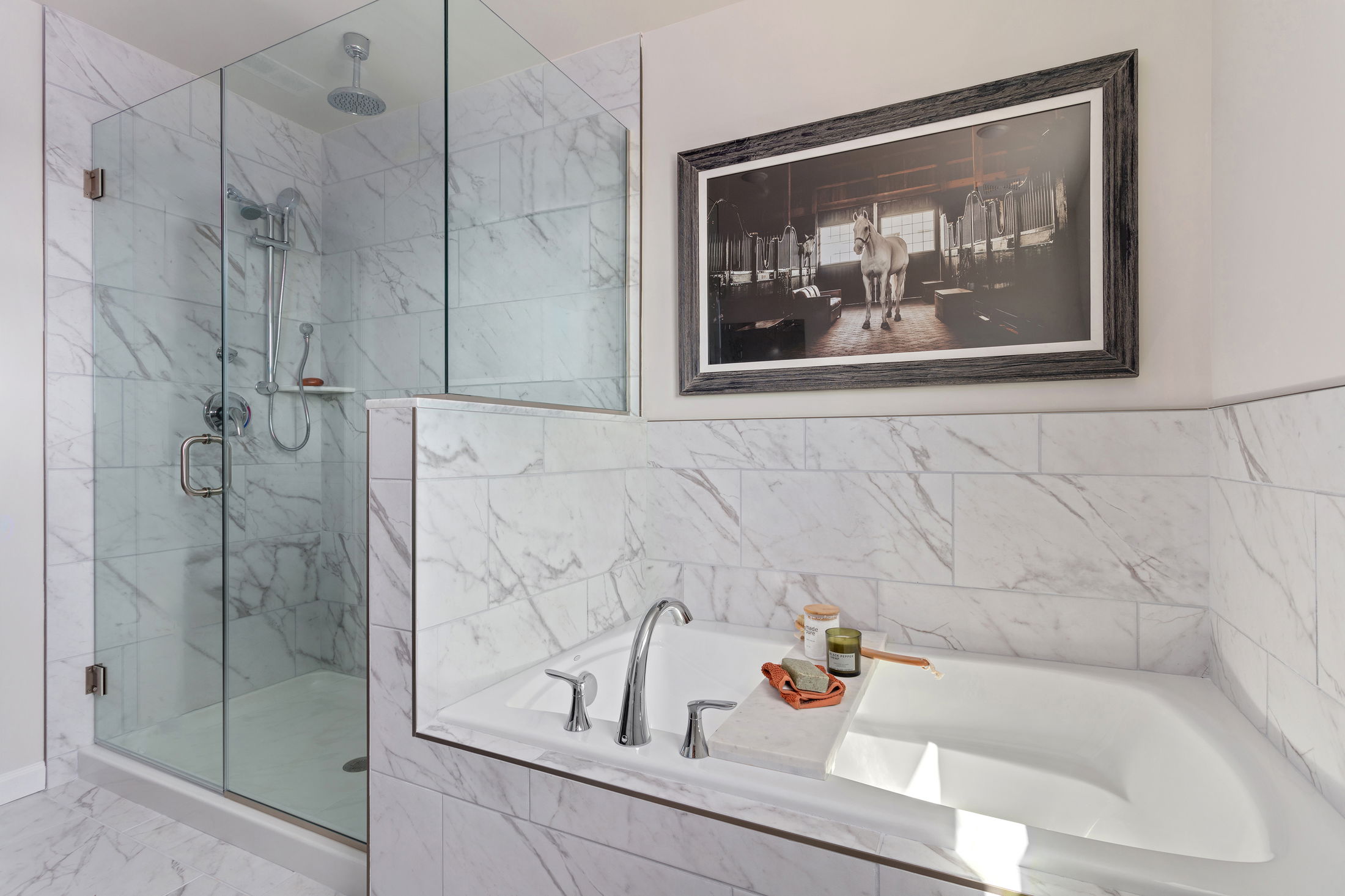 Luxurious bathroom featuring a glass-enclosed marble shower and a sleek bathtub adorned with candles and toiletries.