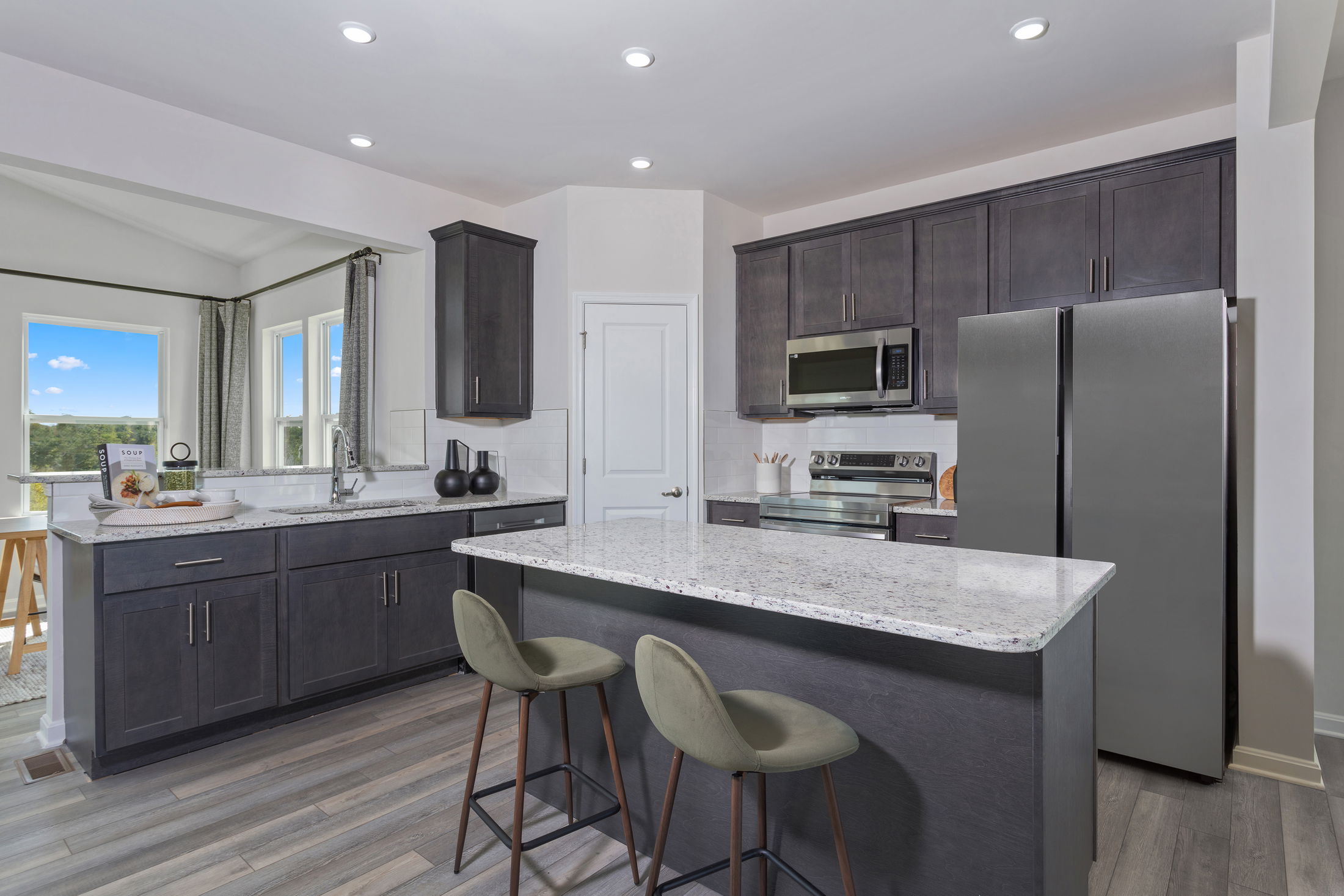 Modern kitchen with dark cabinets, stainless steel appliances, and a spacious granite island with bar stools.
