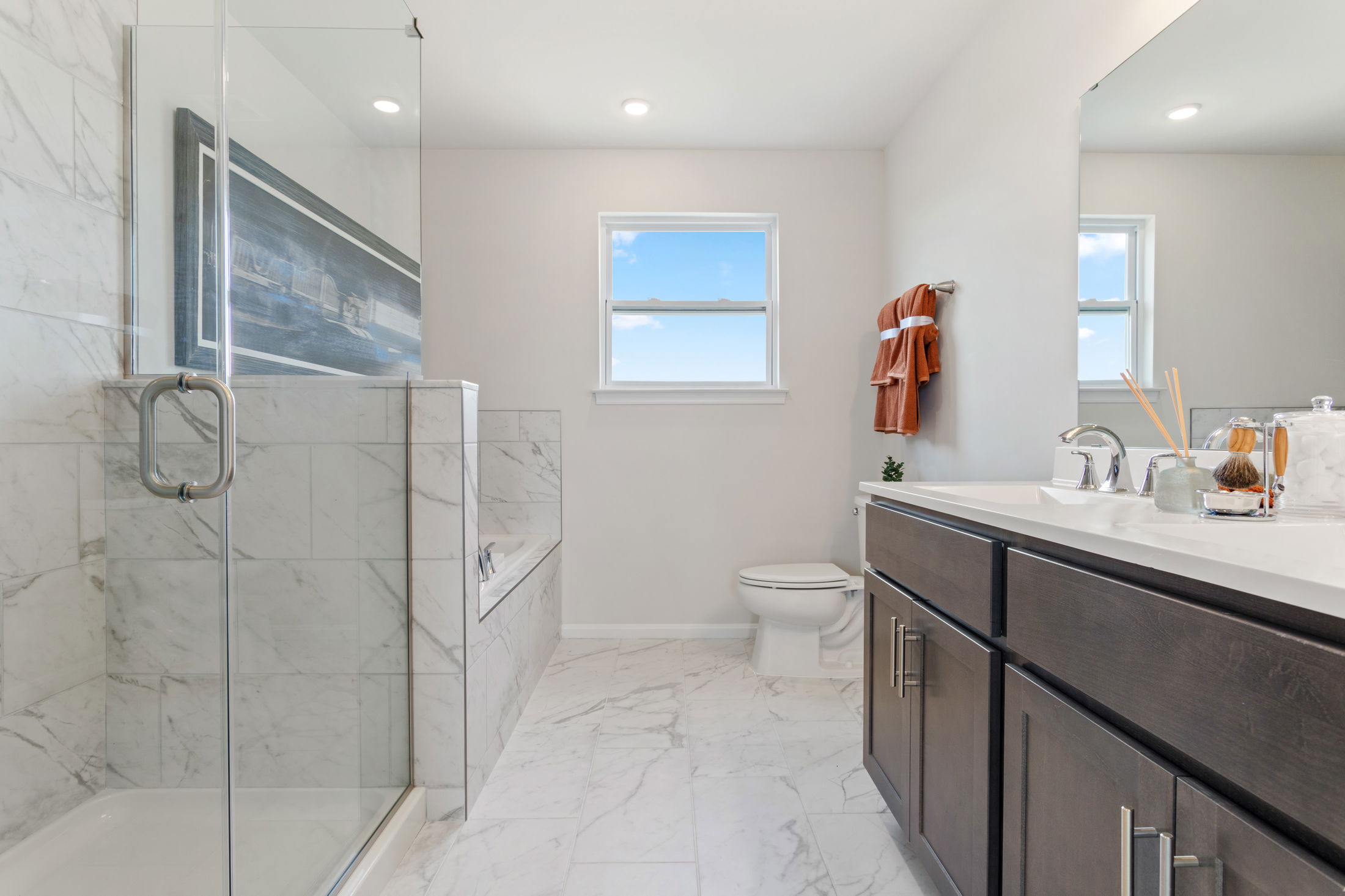 Modern bathroom with glass shower, marble tiles, and a sleek dark wood vanity.