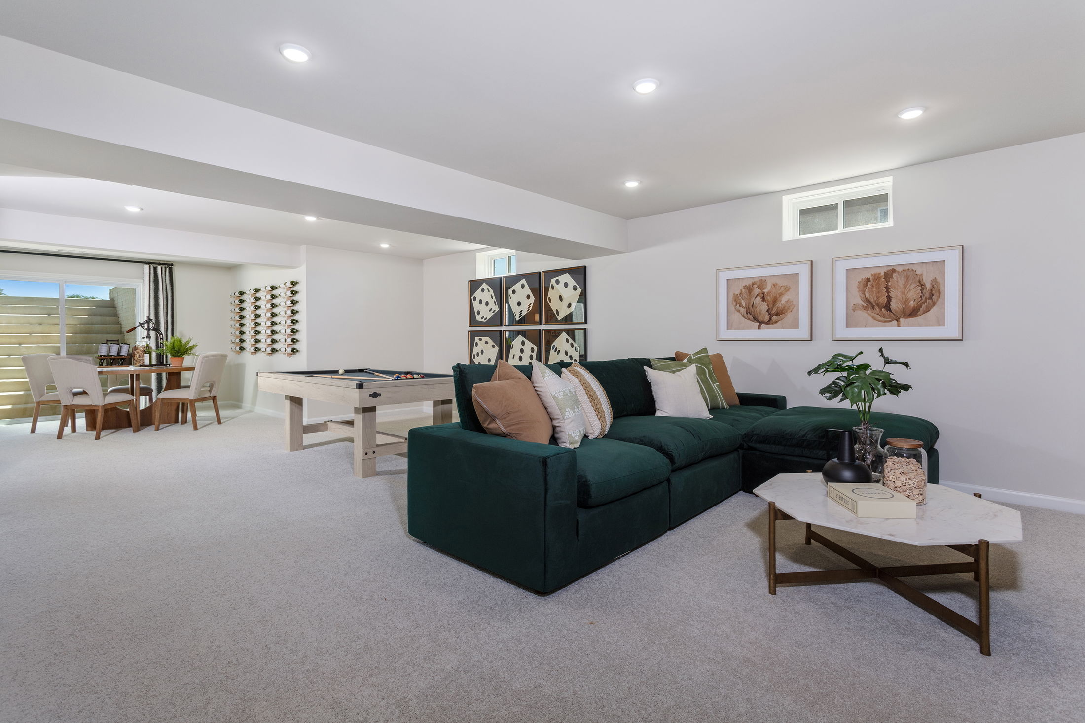 Modern basement living area with a green sectional sofa, pool table, and dining space.