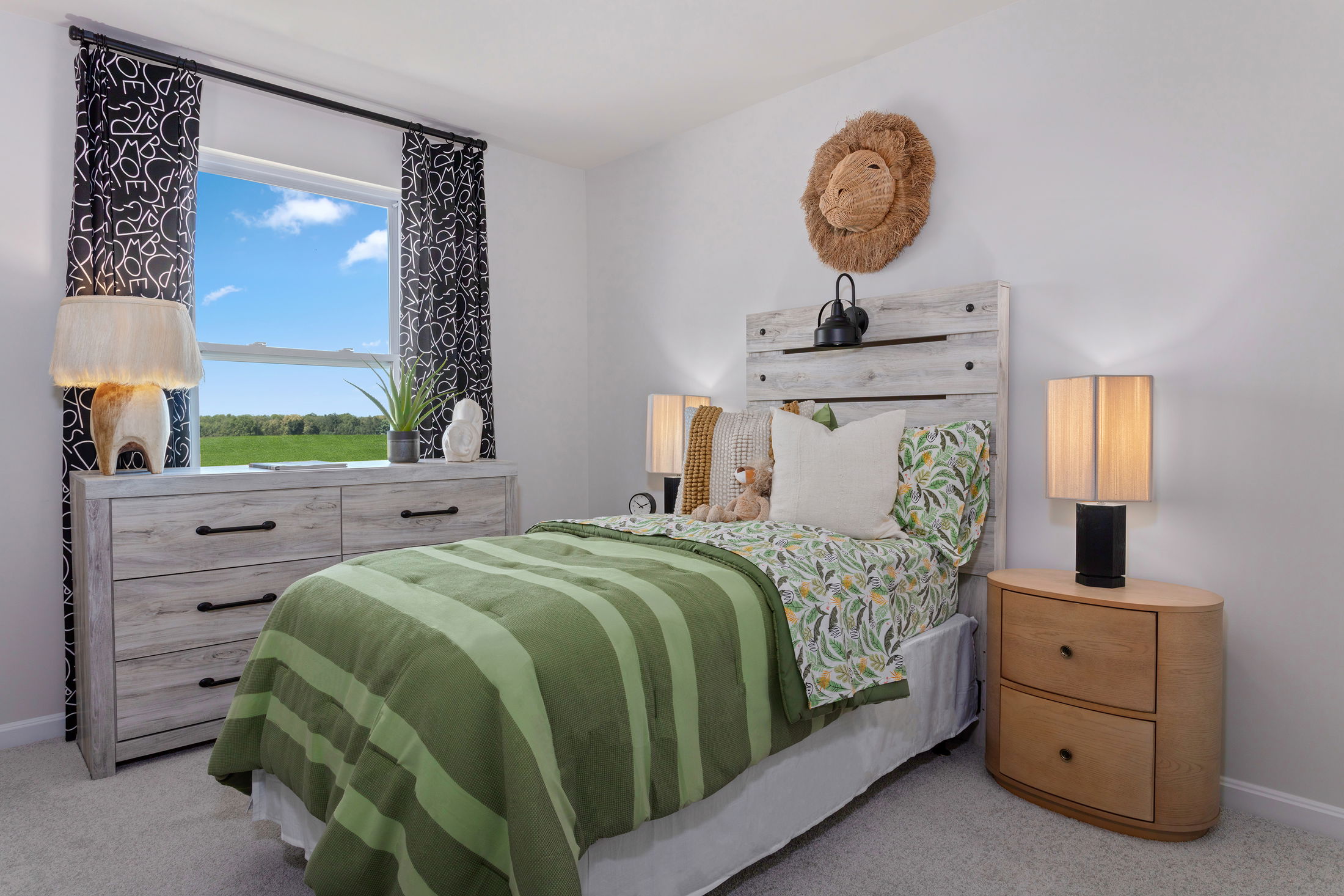 Cozy children's bedroom with a green-themed bed, wooden furniture, and a window view of a lush landscape.