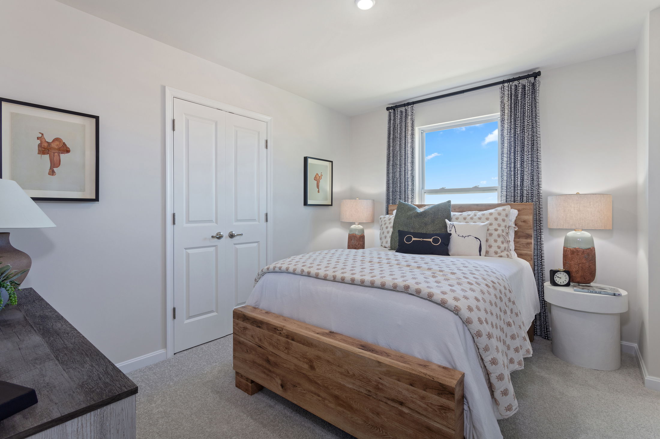 Contemporary bedroom with wooden bed frame, decorative pillows, and natural light from a window with patterned curtains.
