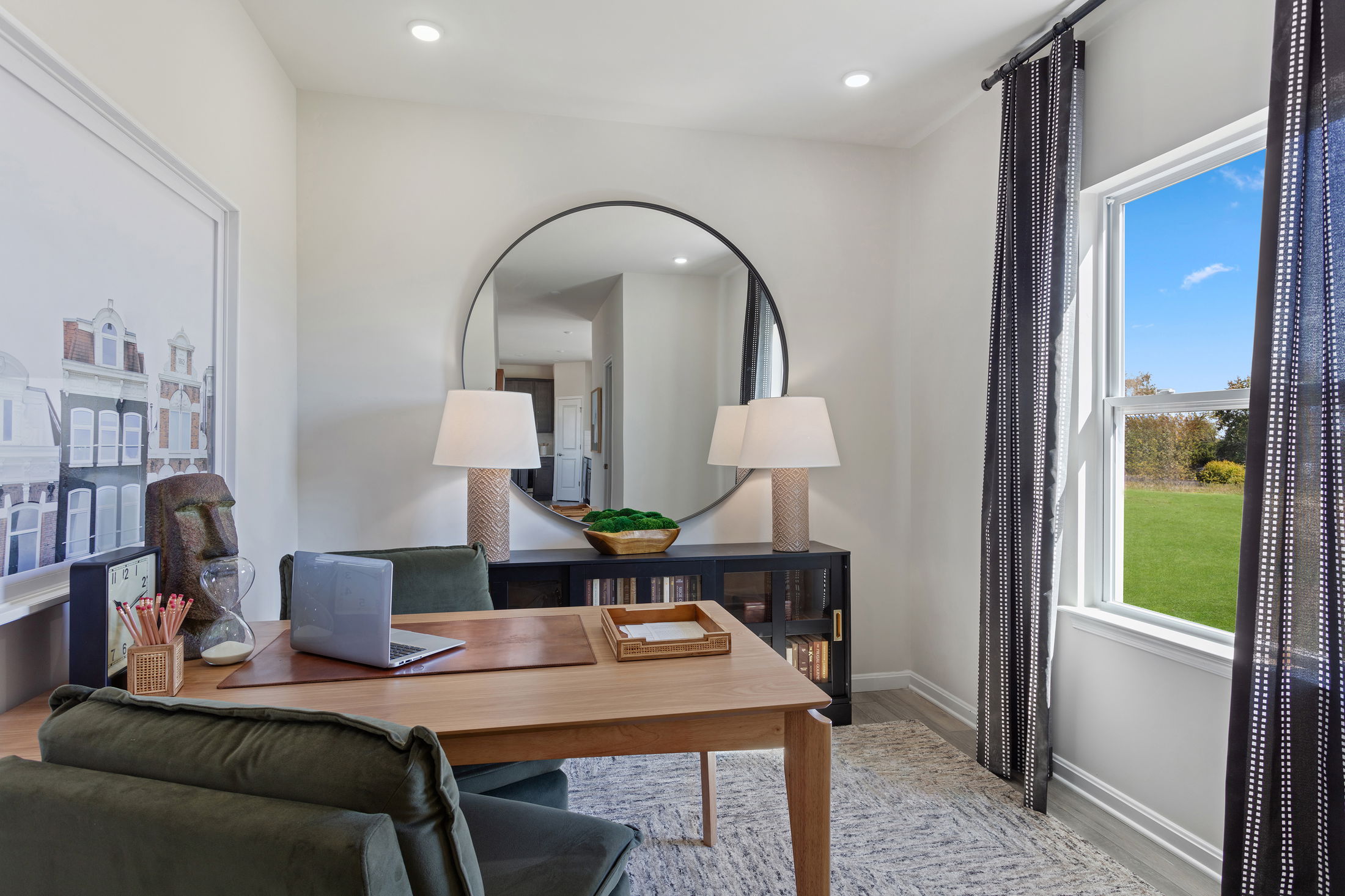 Stylish modern home office with a wooden desk, laptop, and large round mirror reflecting lamps, creating a cozy and efficient workspace.