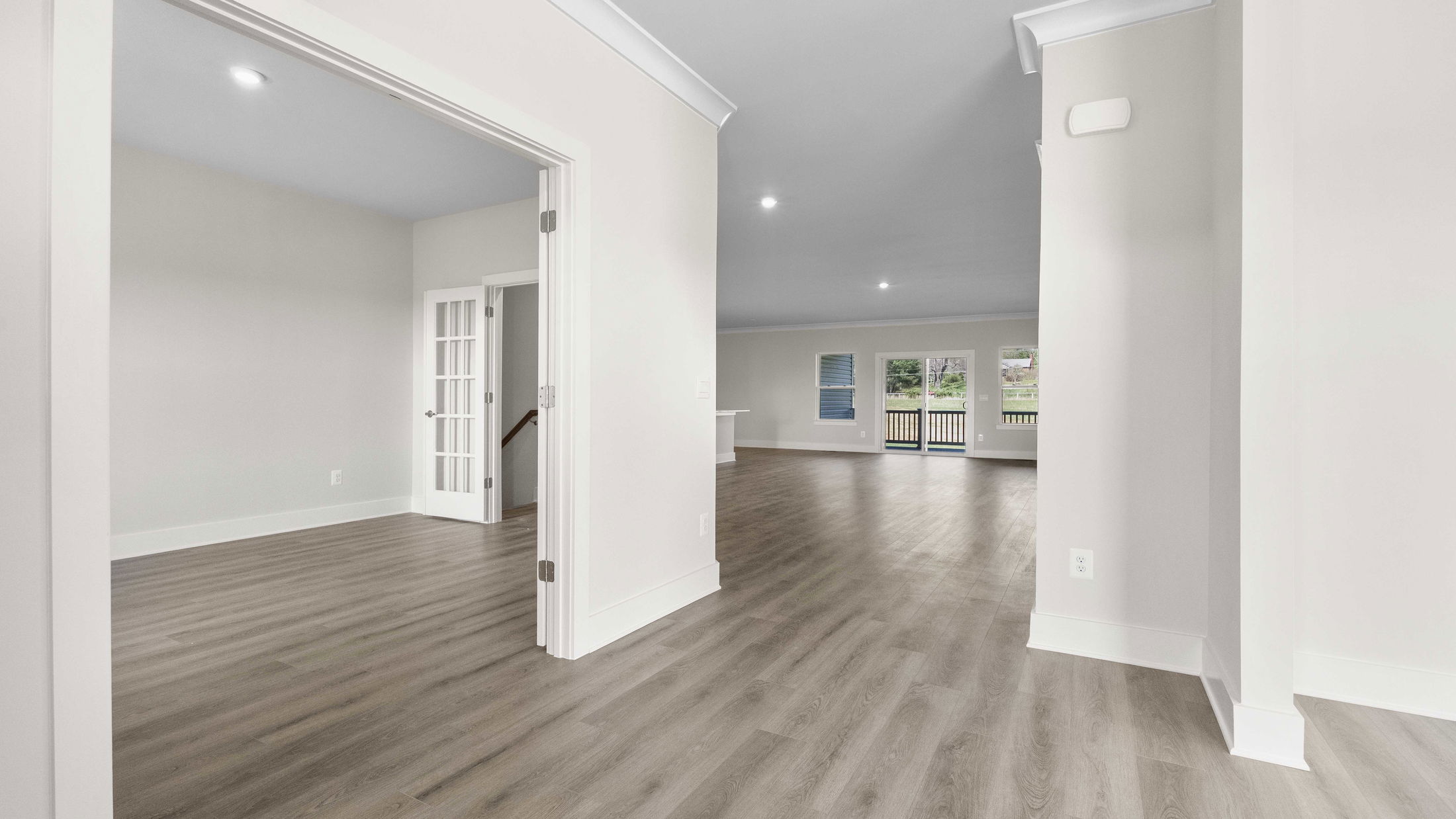 Spacious modern interior with light gray walls, wood flooring, and French doors leading to a bright living area.