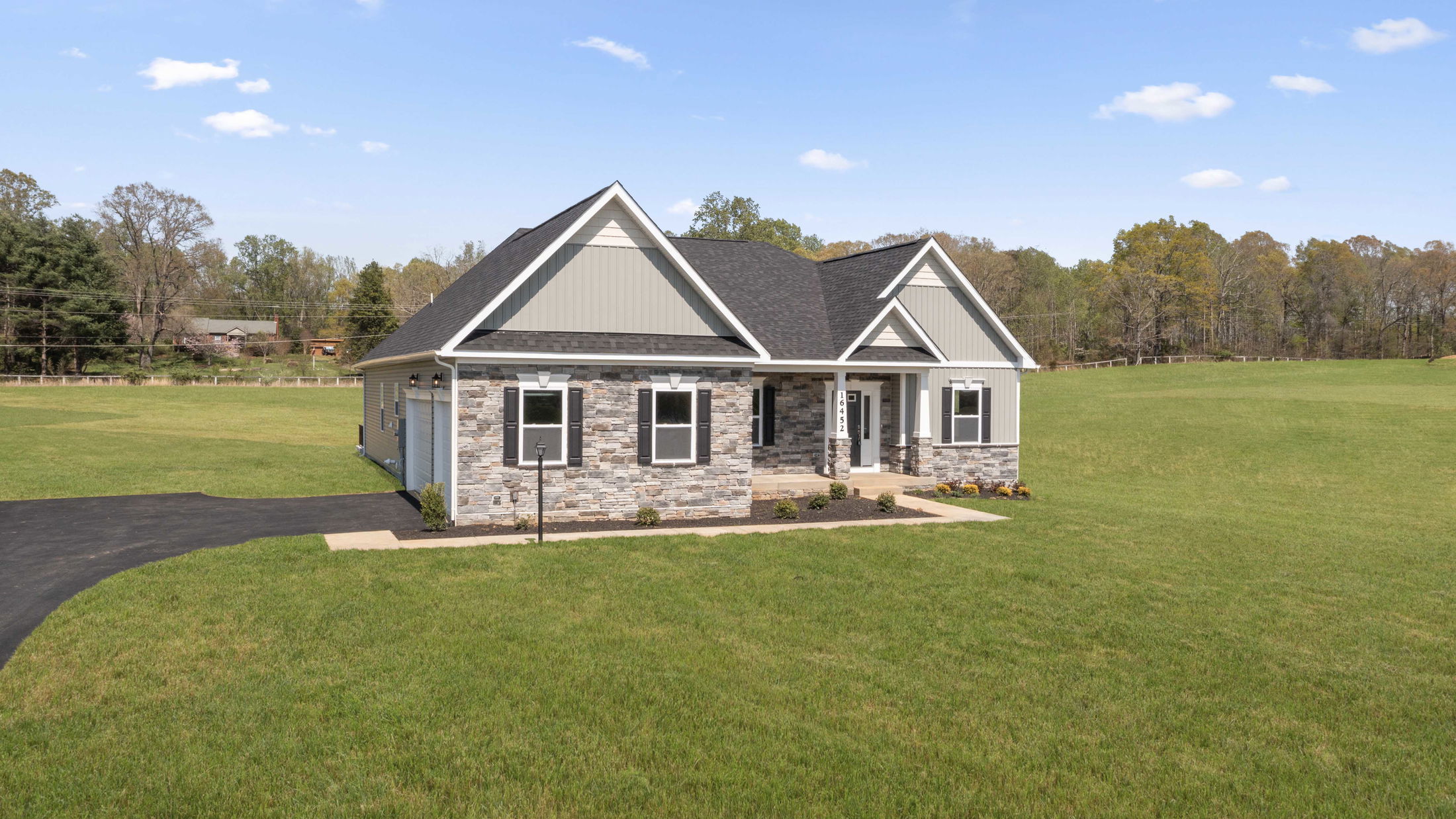 Modern ranch-style house with stone and siding exterior, surrounded by a large green yard and clear blue sky.