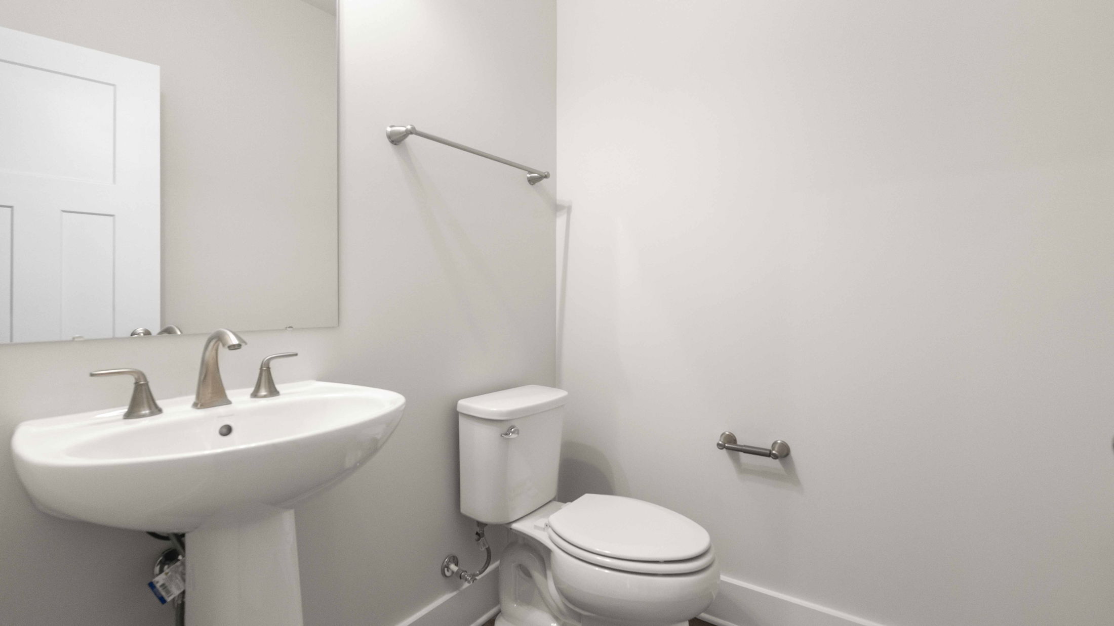 A clean, modern bathroom with a pedestal sink, mirror, and toilet against a white wall.